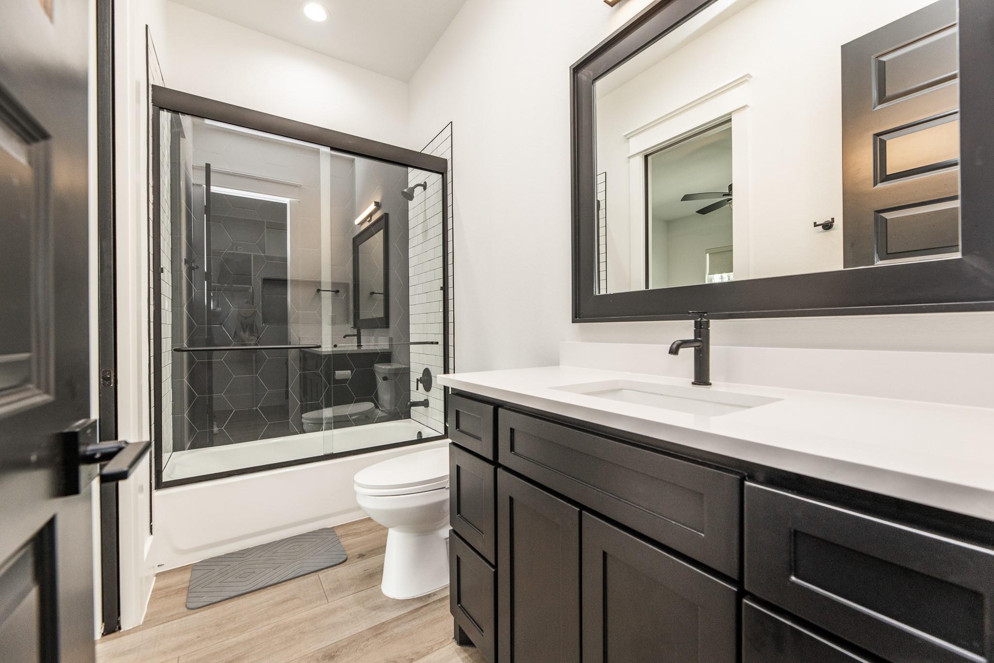 Modern bathroom with a glass-enclosed tub and shower, dark hexagonal tile, and a wide dark vanity.
