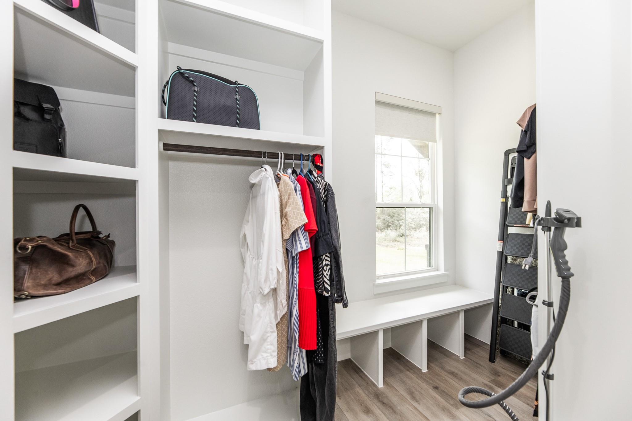 Walk-in closet with built-in shelving, hanging clothes, a window, and wood-look flooring.