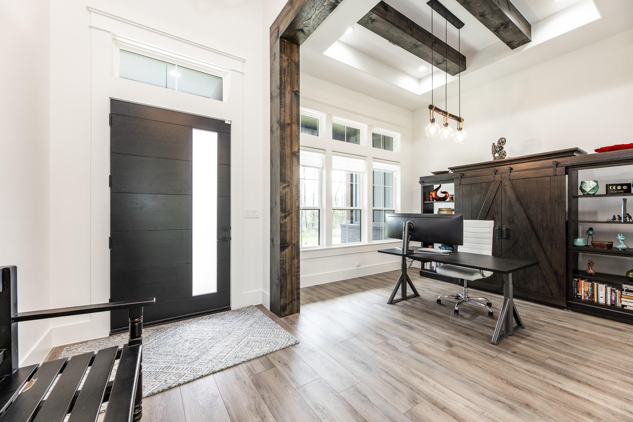 Home office with dark wood built-ins, a desk, large windows, and a black front door.