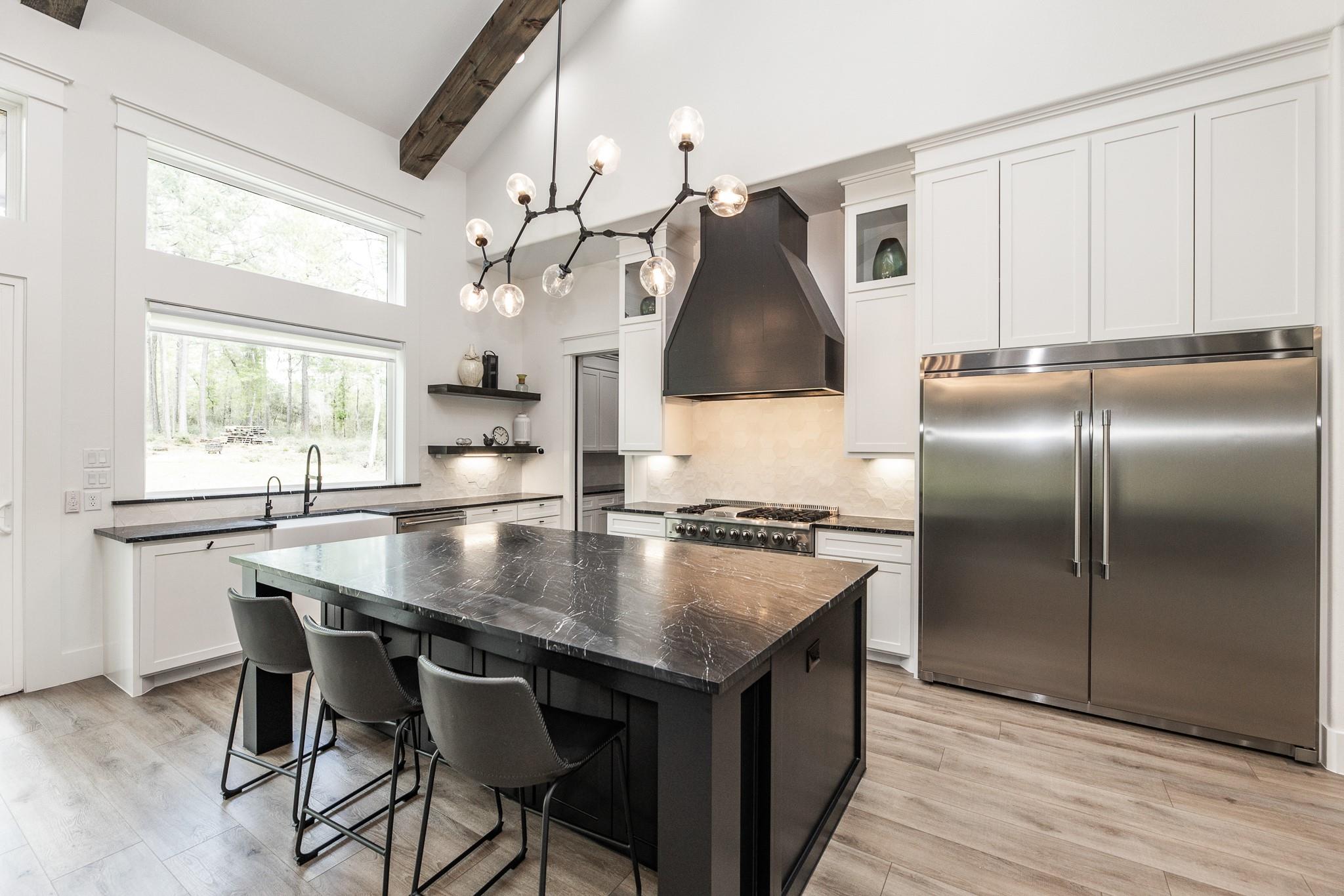 Modern kitchen with a dark stone island, white cabinetry, stainless steel appliances, and vaulted ceiling.