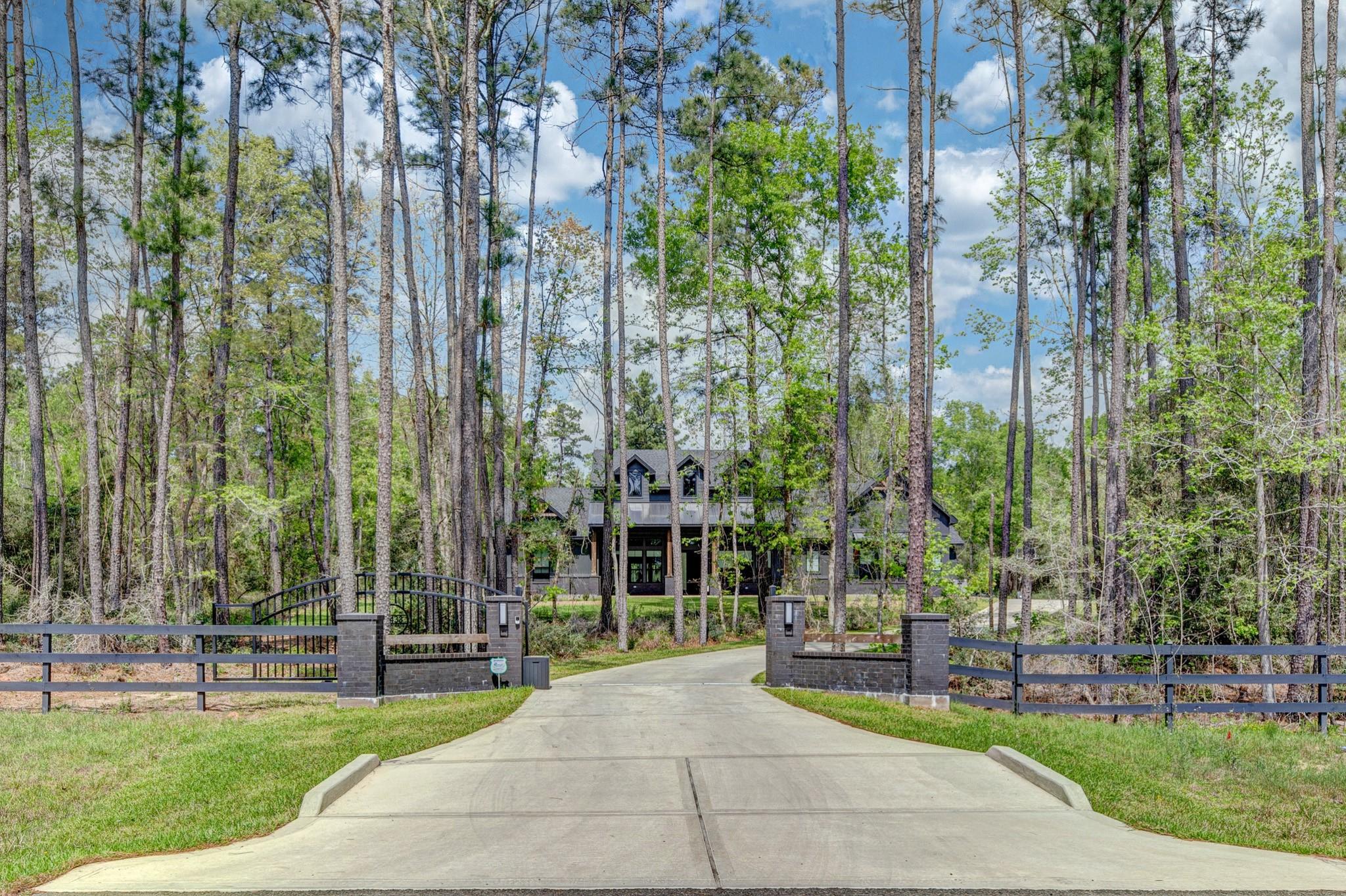 Wooded home at the end of a concrete driveway, seen through an open gate.