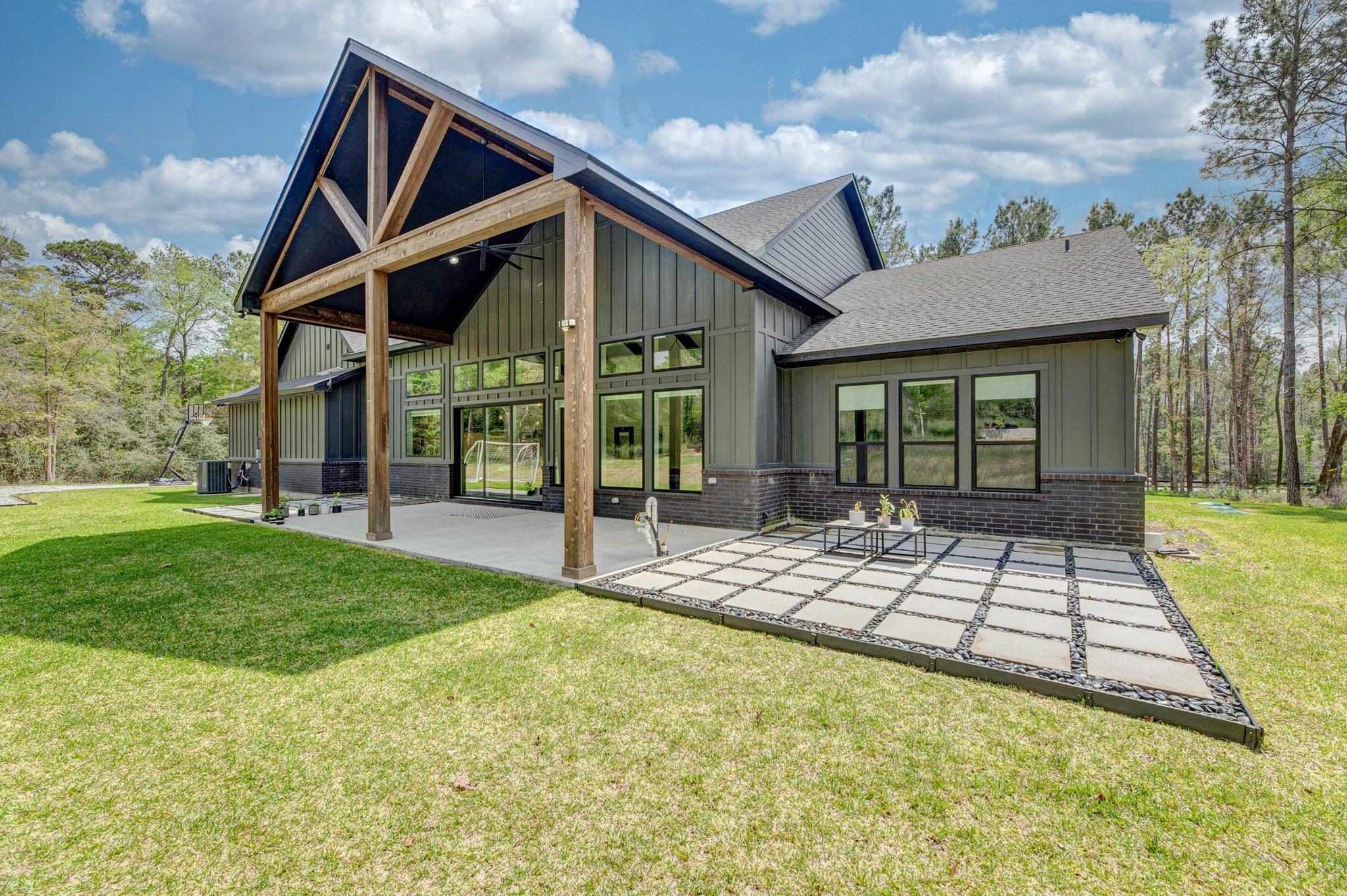 Modern gray home with a timber-truss covered patio and geometric paver terrace.