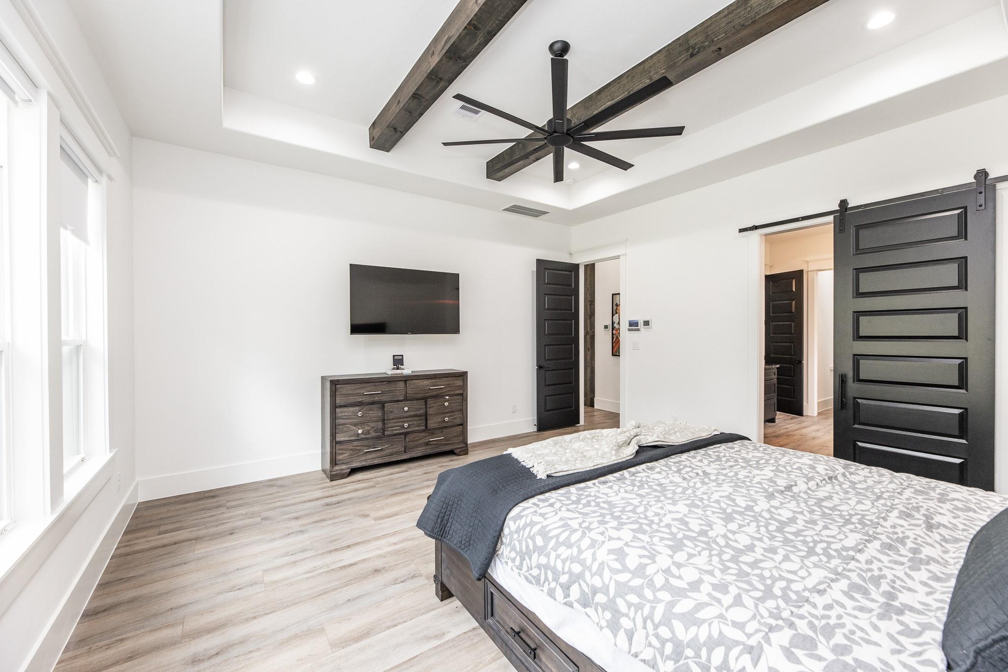 Bedroom with exposed wood ceiling beams, a large fan, and dark barn doors beside the bed.