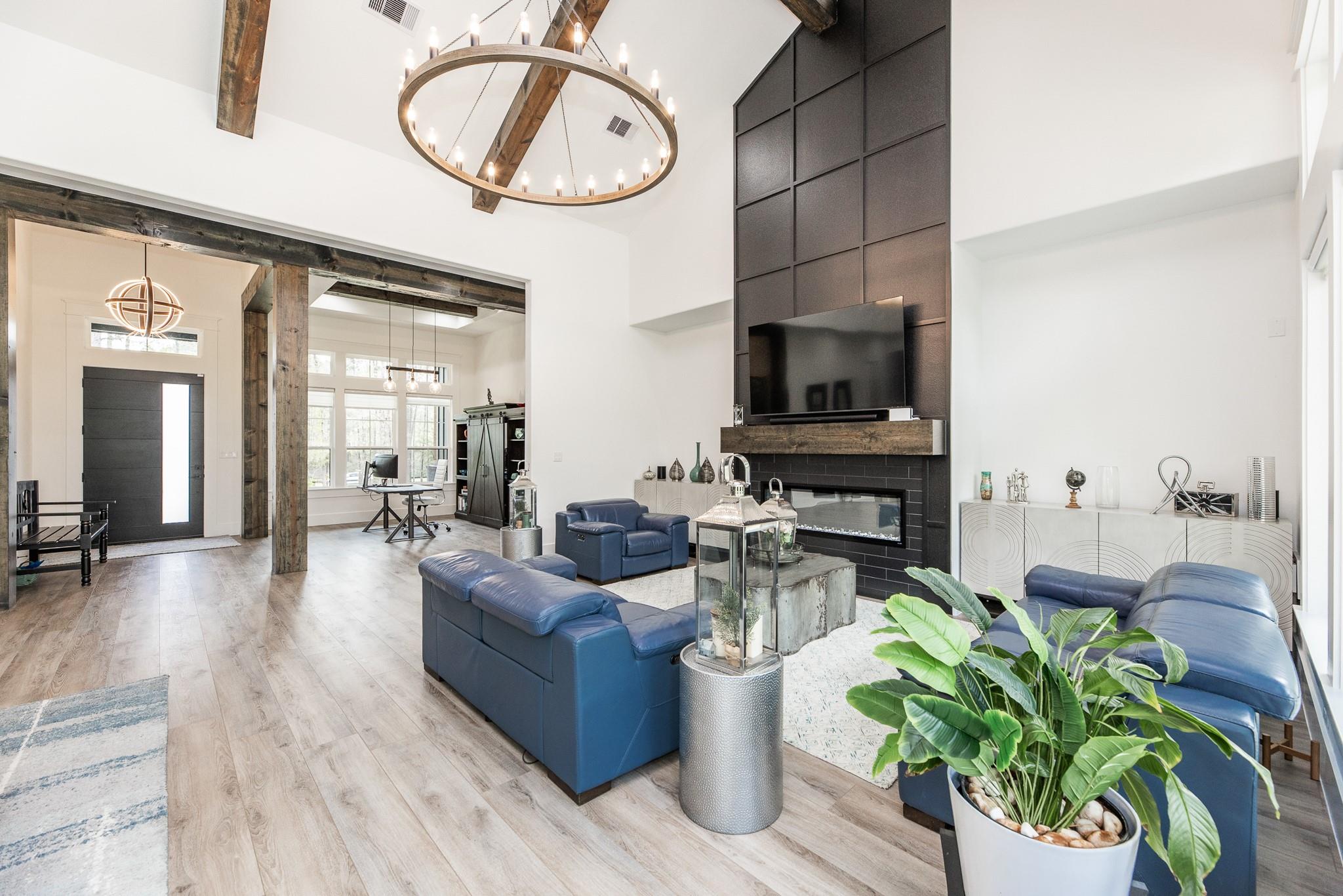 Living room with blue leather sofas, a tall tiled fireplace, exposed beams, and a circular chandelier.