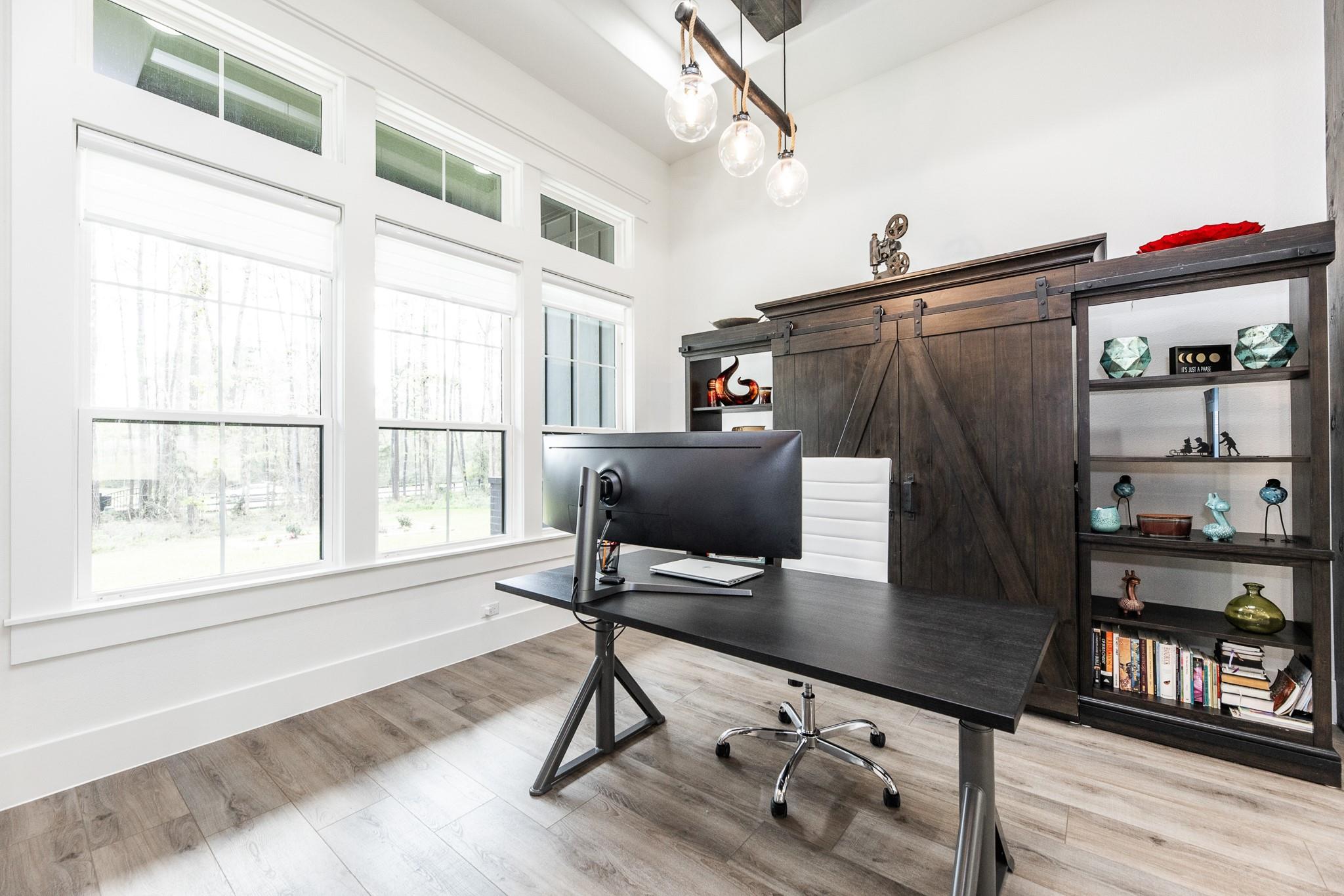 Furnished home office with a black desk, dark barn-door shelving, and tall windows.