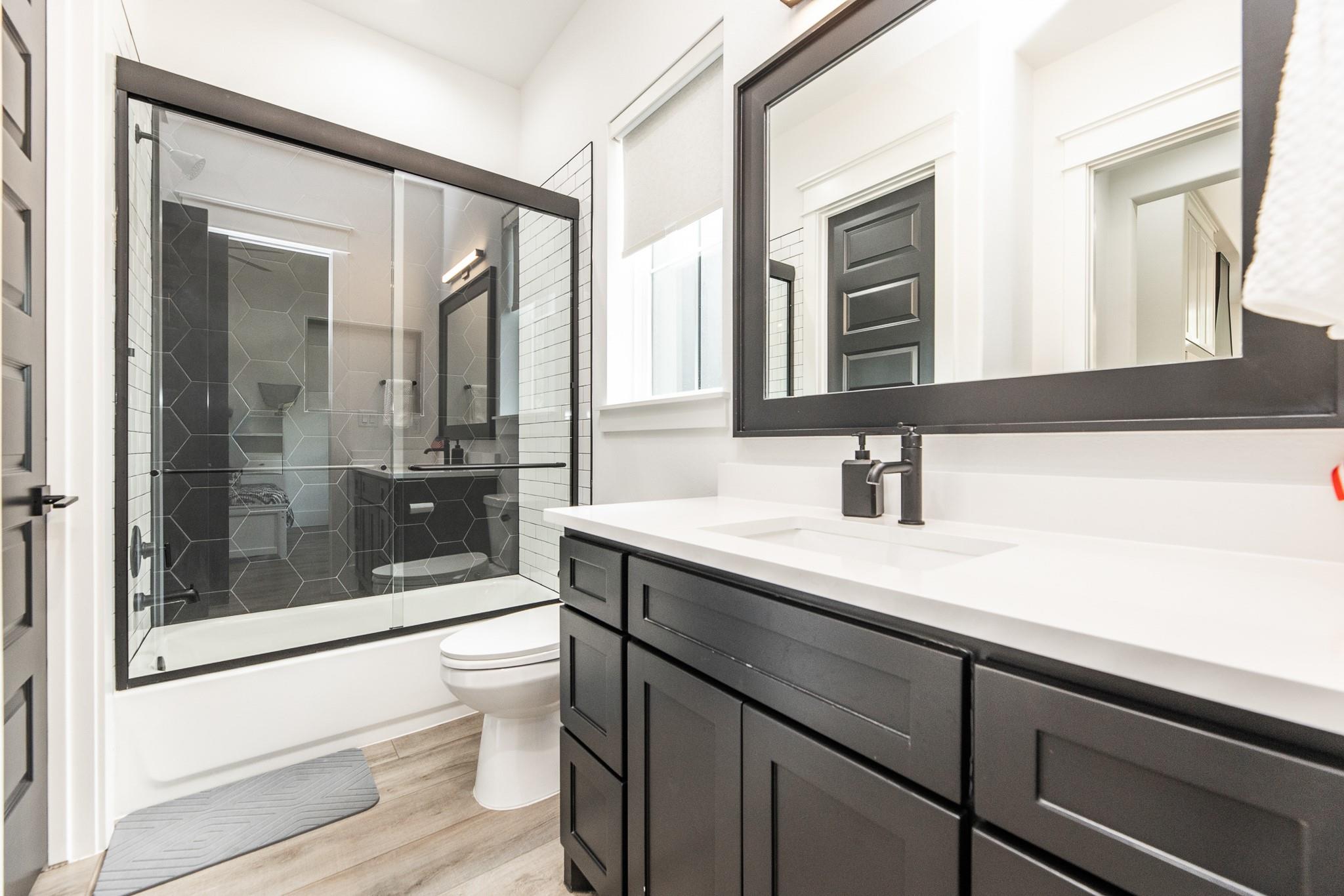 Bathroom with a dark geometric-tile walk-in shower and black vanity with white countertop.