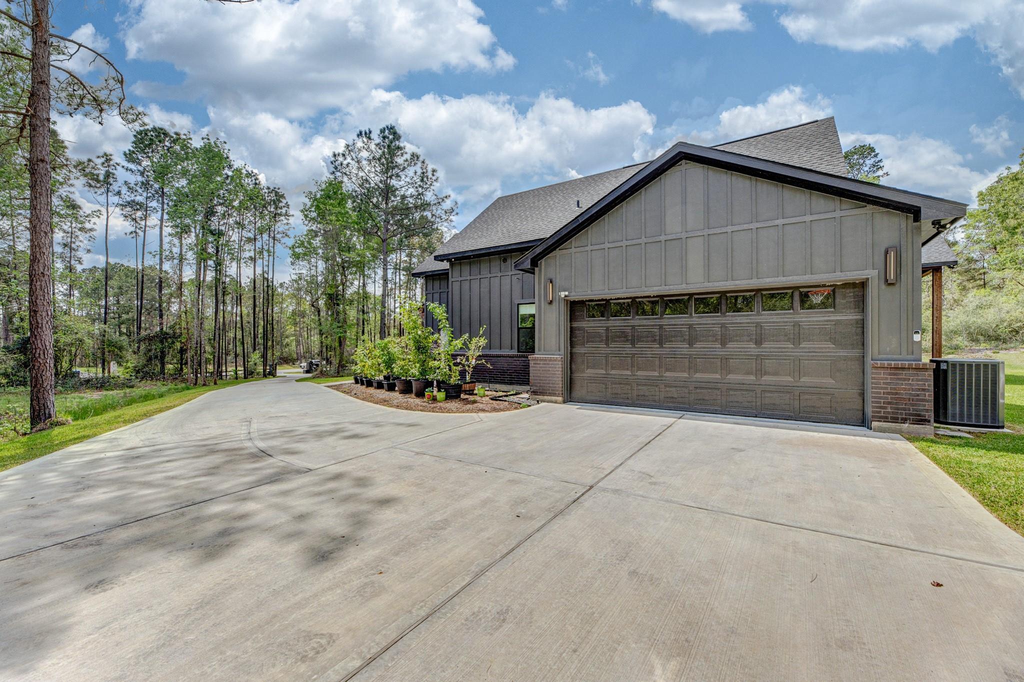 Modern gray house with a wide garage and basketball hoop beside a wooded driveway.