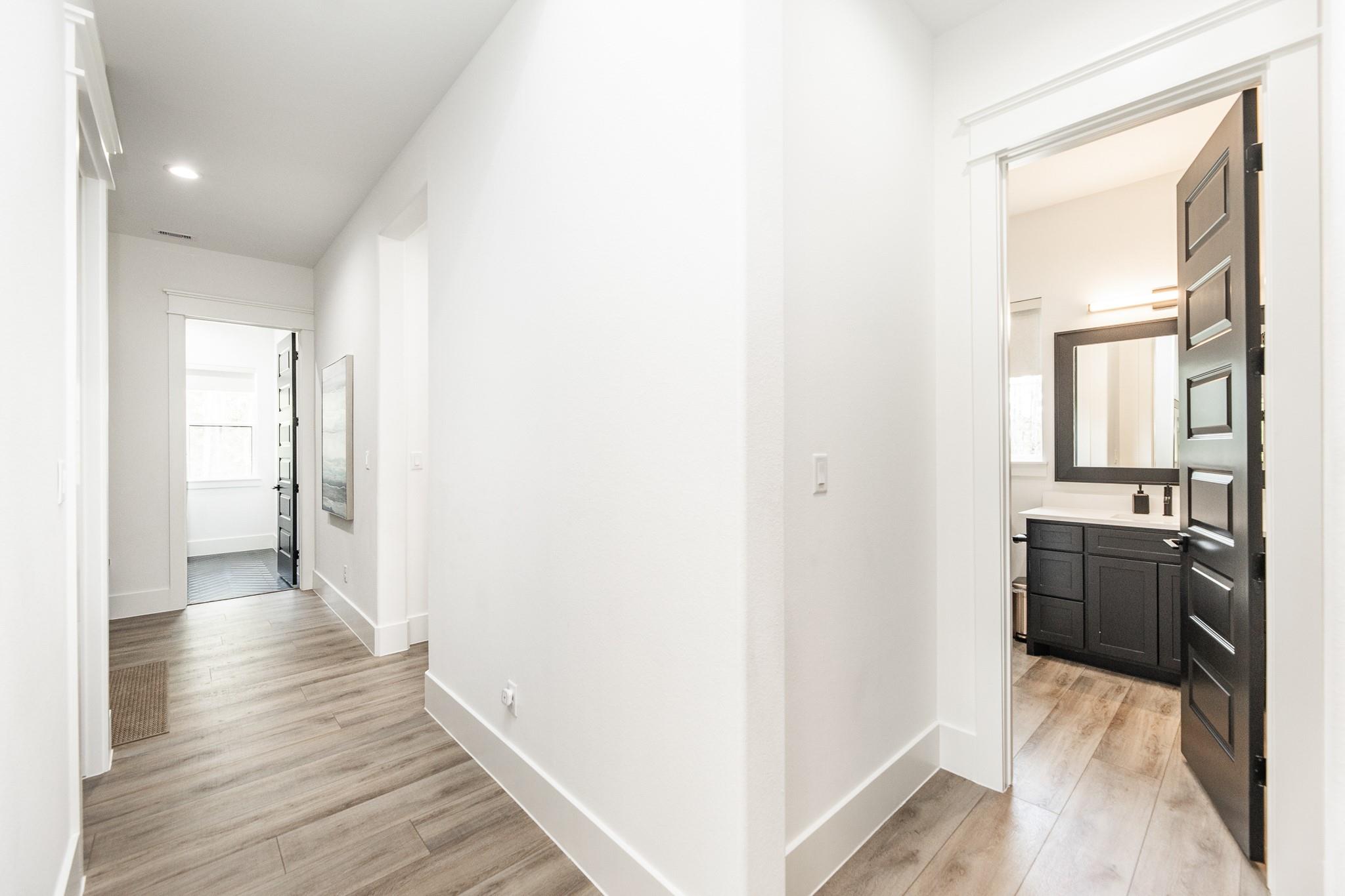 Bright hallway with wood-look flooring and open black doors revealing a bathroom vanity.
