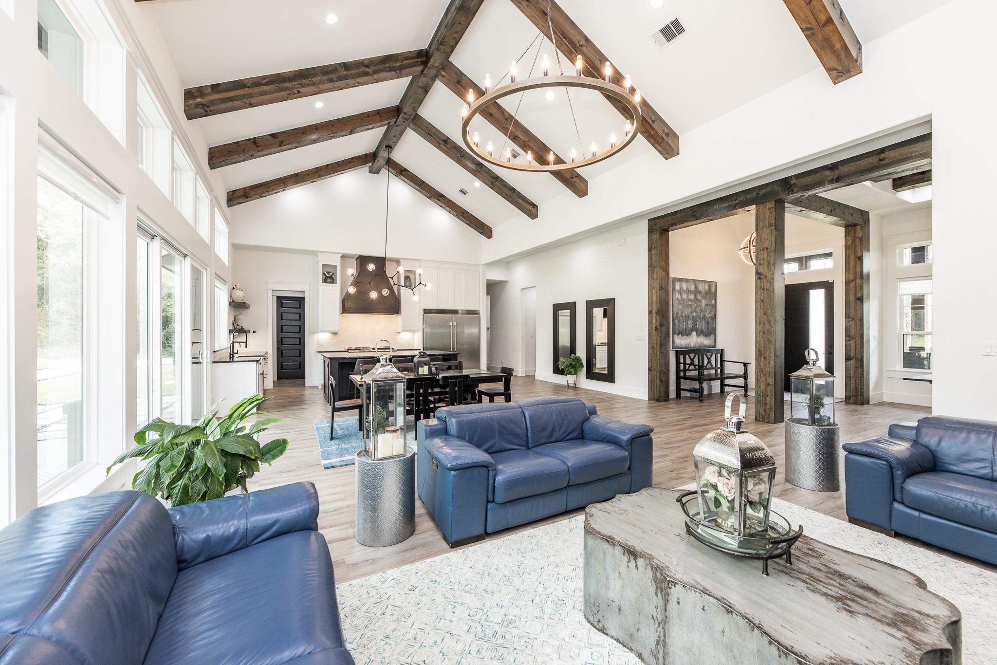 Open-plan living room with blue leather sofas, exposed wood ceiling beams, and a kitchen-dining area.