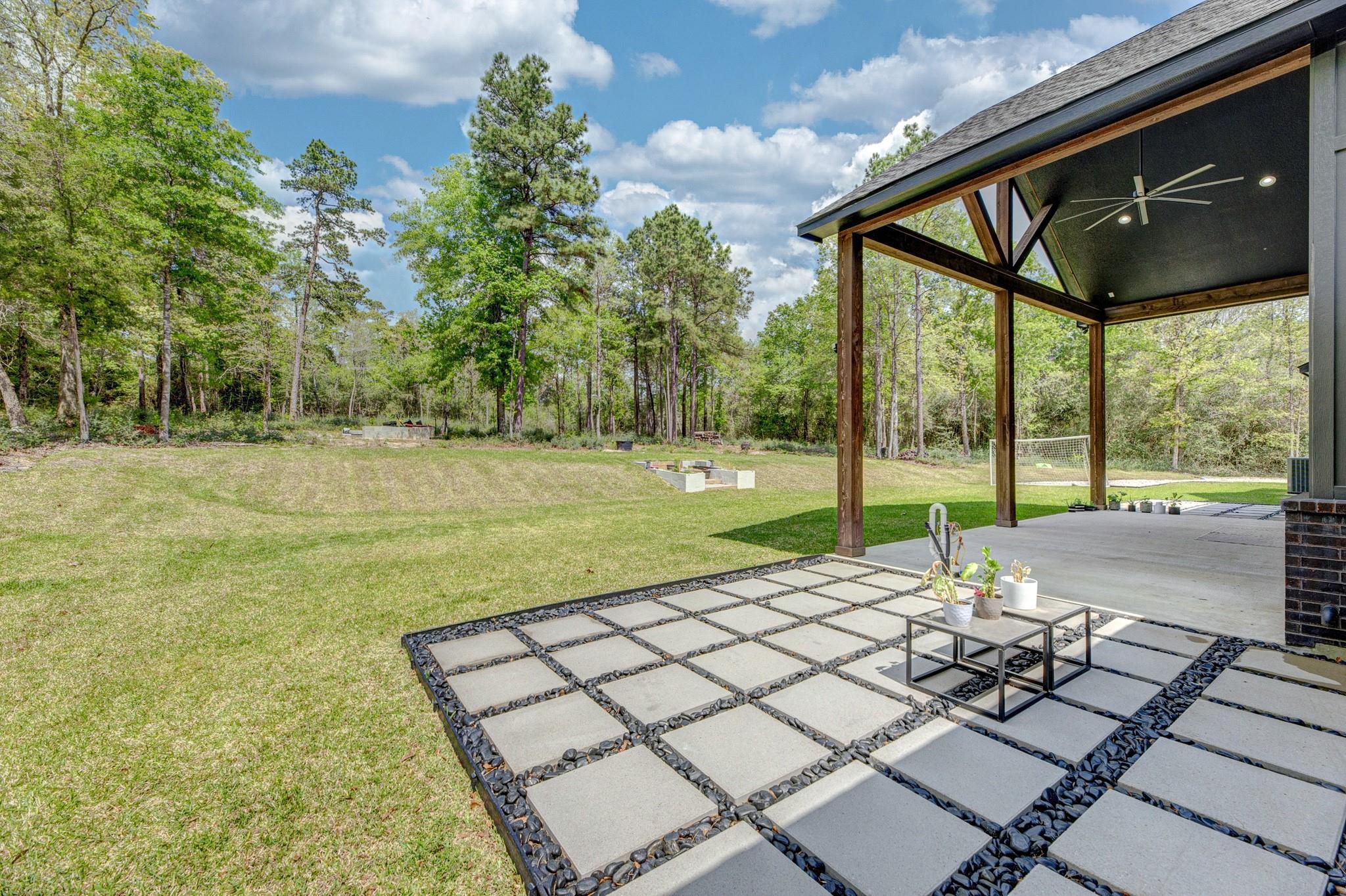Covered patio with a paver terrace overlooking a spacious grassy backyard and trees.