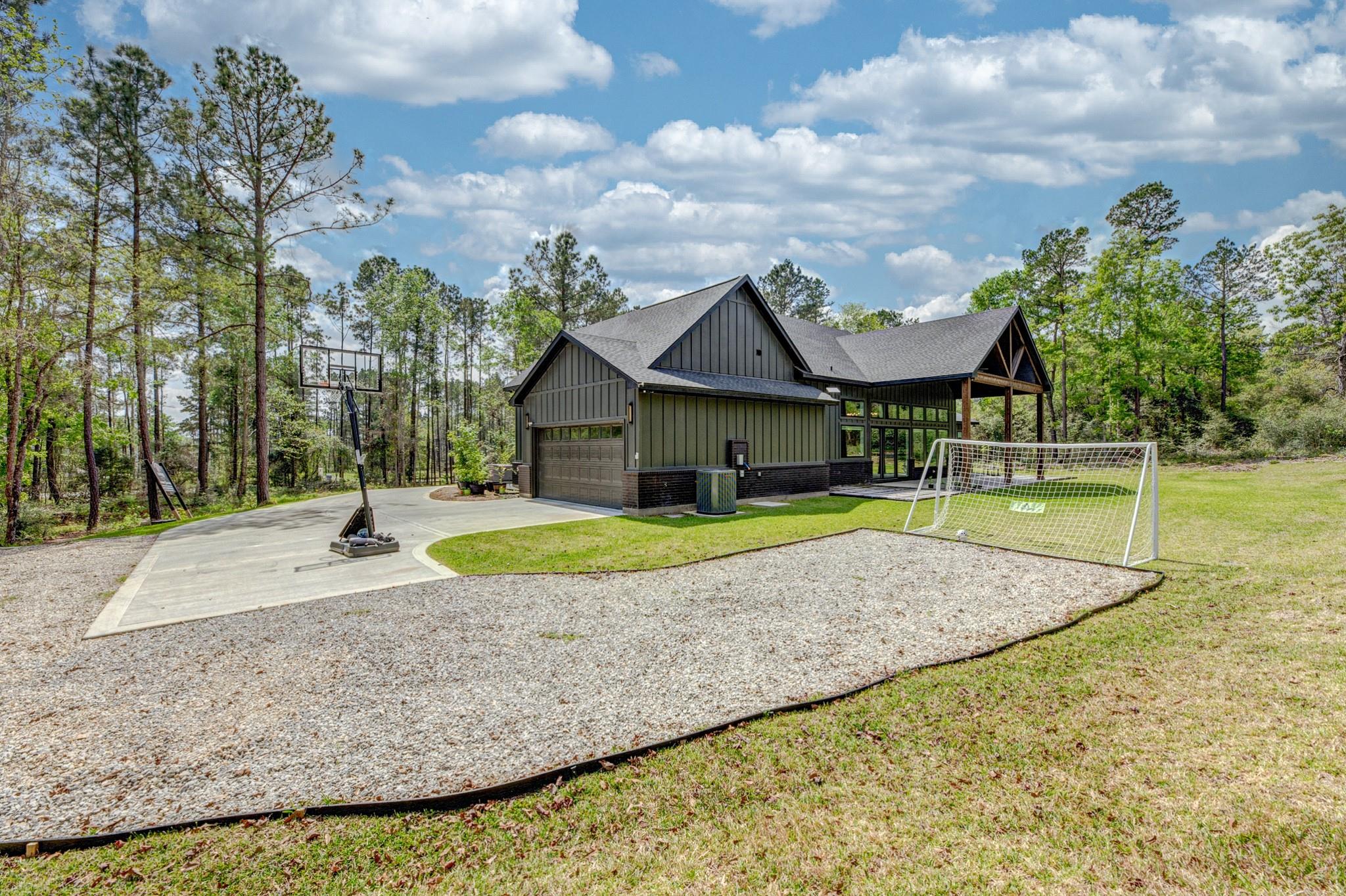 Dark-sided home with a covered porch, wooded surroundings, basketball hoop, and soccer goal.