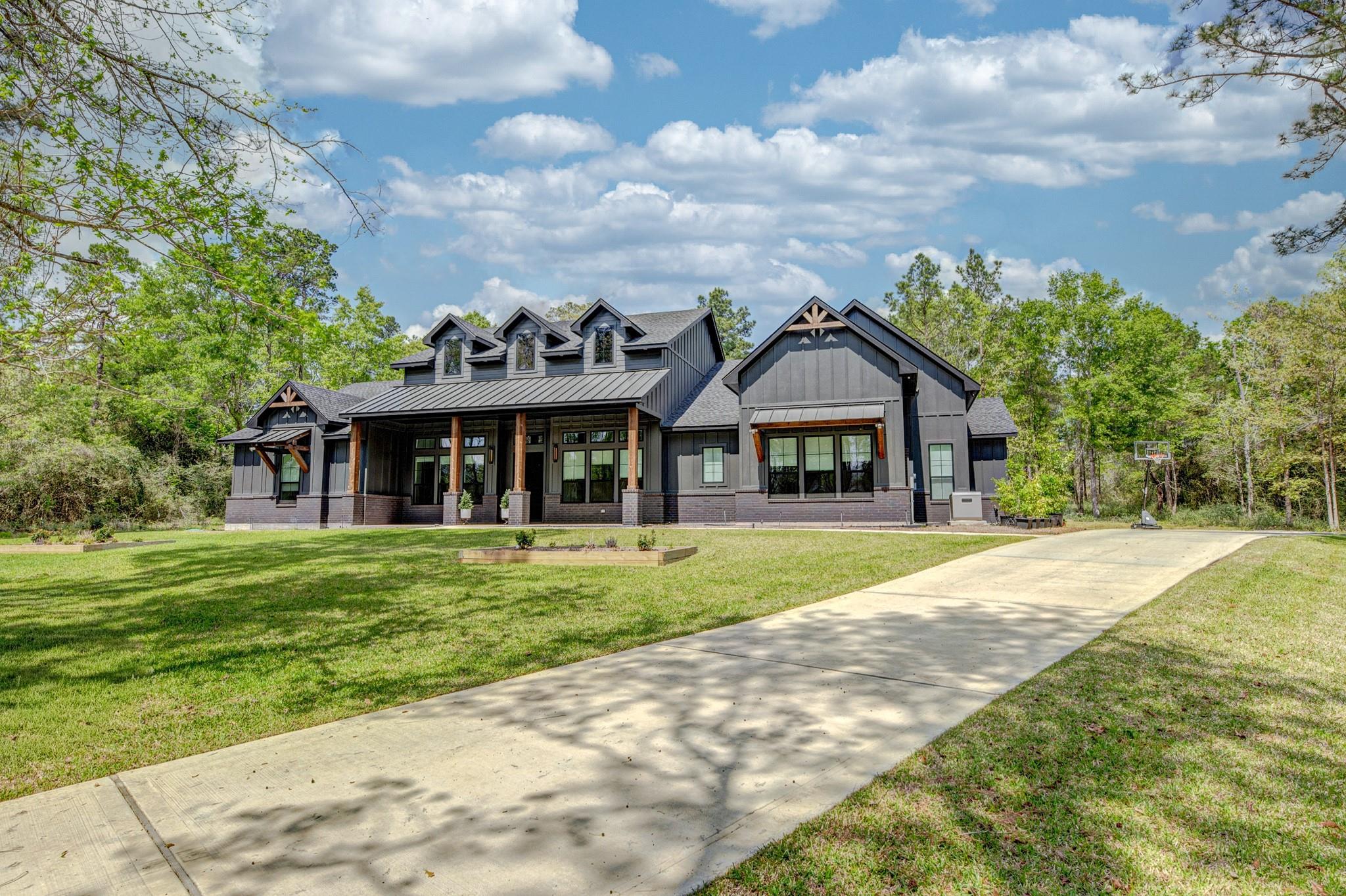 Modern gray farmhouse with a covered porch, broad driveway, and basketball hoop beside the lawn.