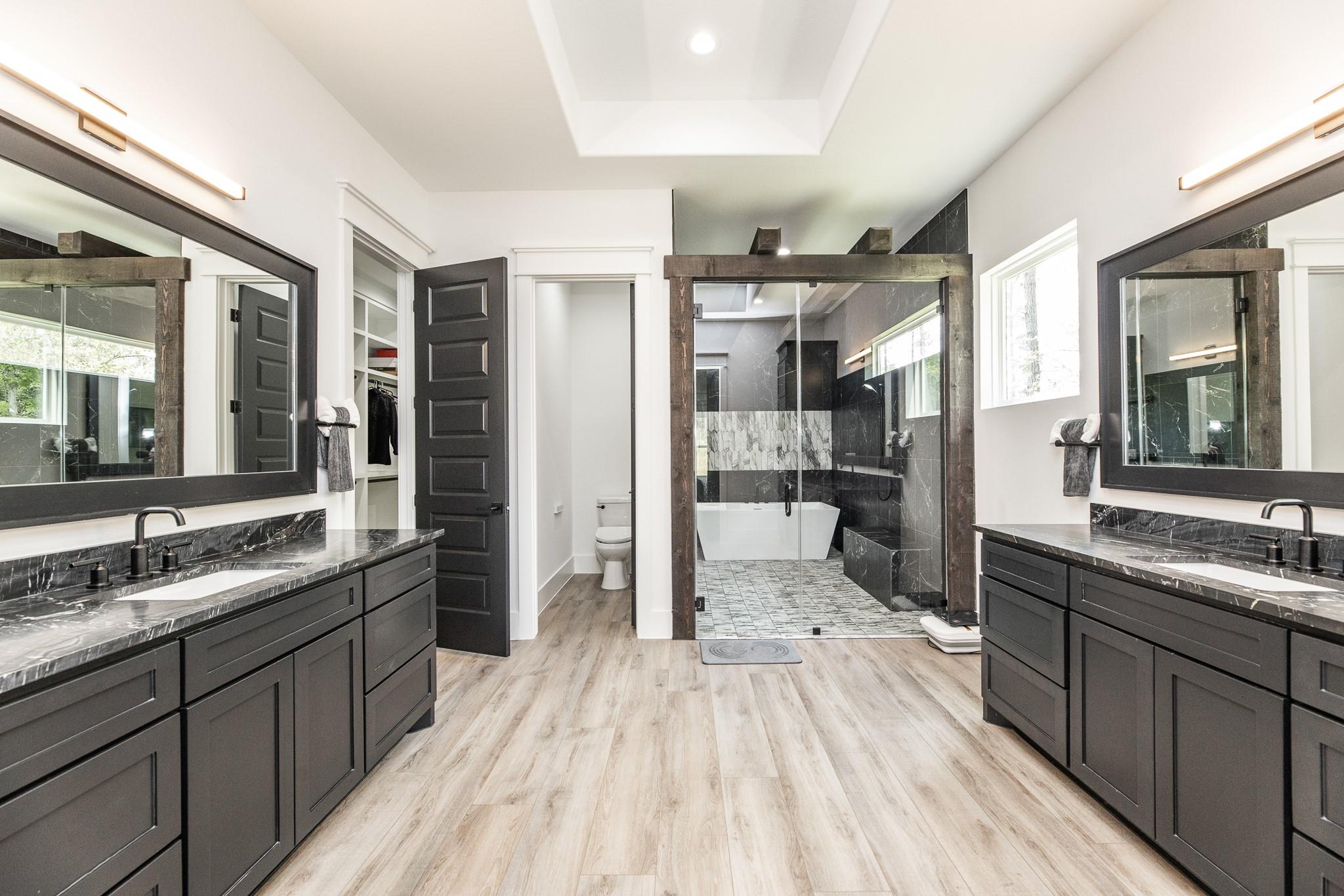 Modern bathroom with double dark vanities, marble countertops, and a glass shower beside a freestanding tub.
