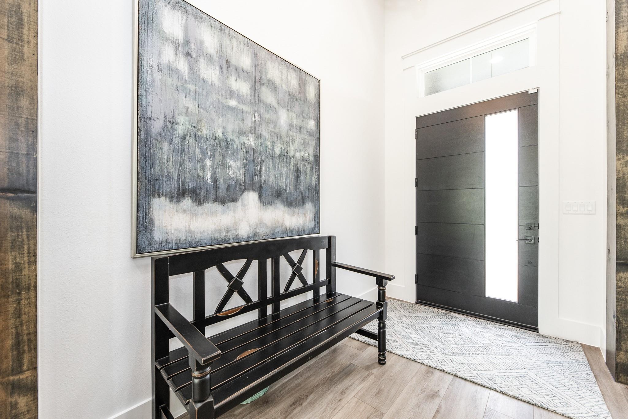 Entryway with a black slatted bench beneath abstract art beside a dark front door with a tall glass panel.