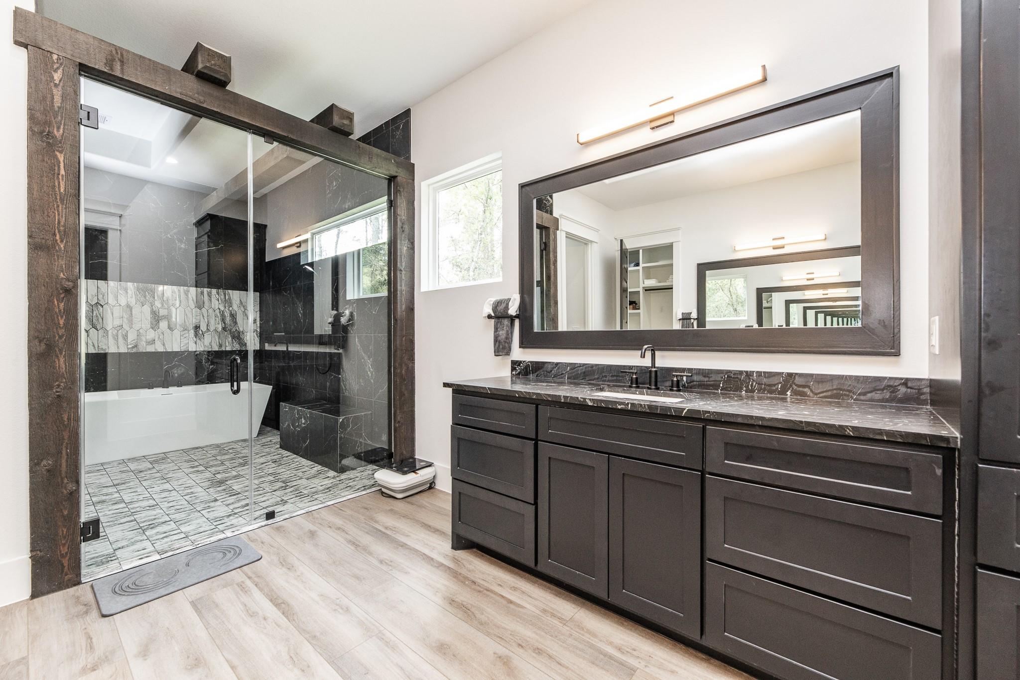 Modern bathroom with glass walk-in shower, freestanding tub, and long dark vanity.