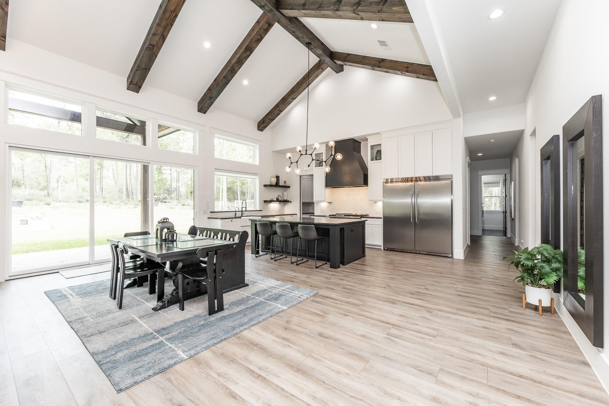 Open kitchen and dining area with vaulted exposed-beam ceiling, dark island, and large windows.