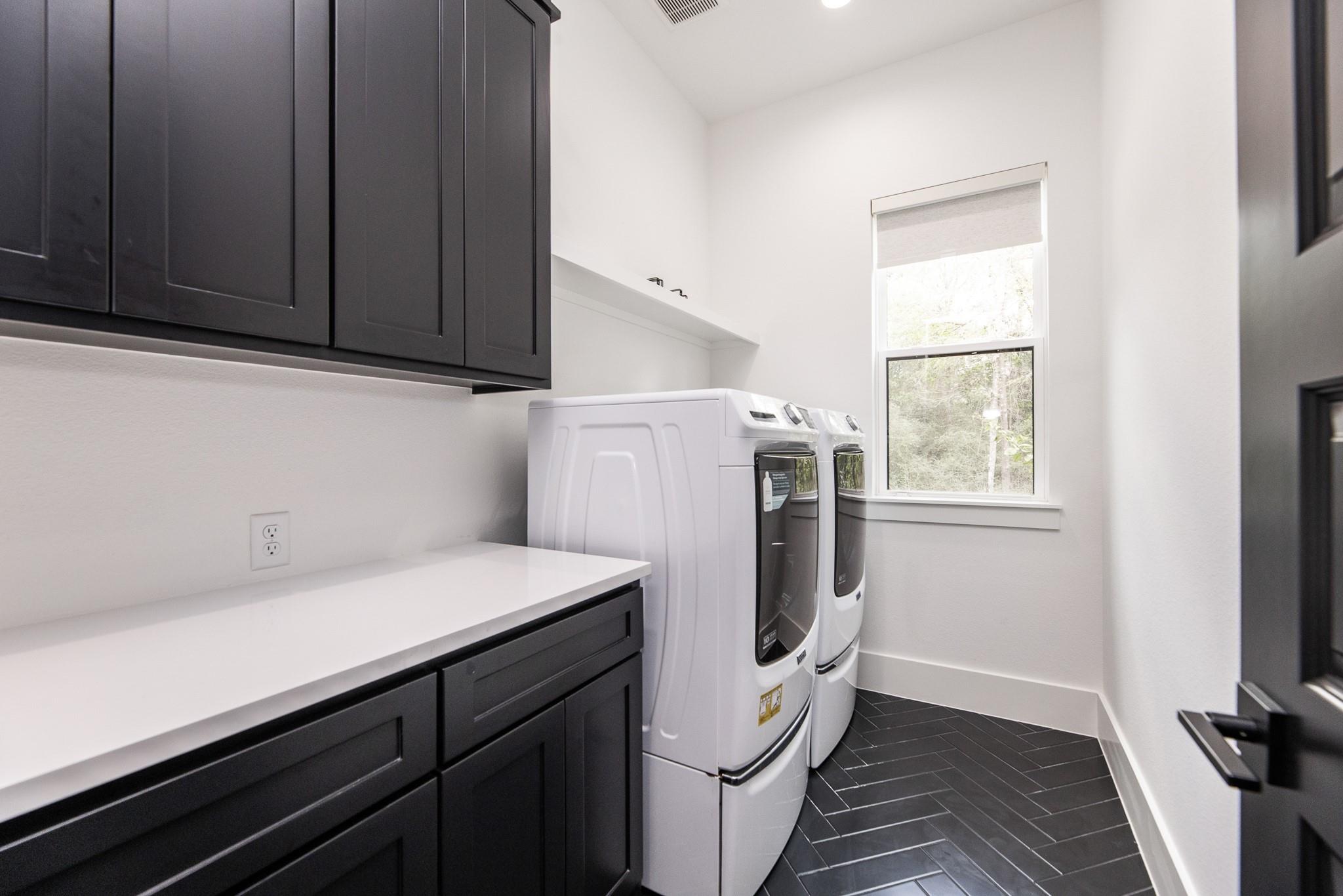 Laundry room with dark cabinetry, white countertop, and washer and dryer beside a tall window.