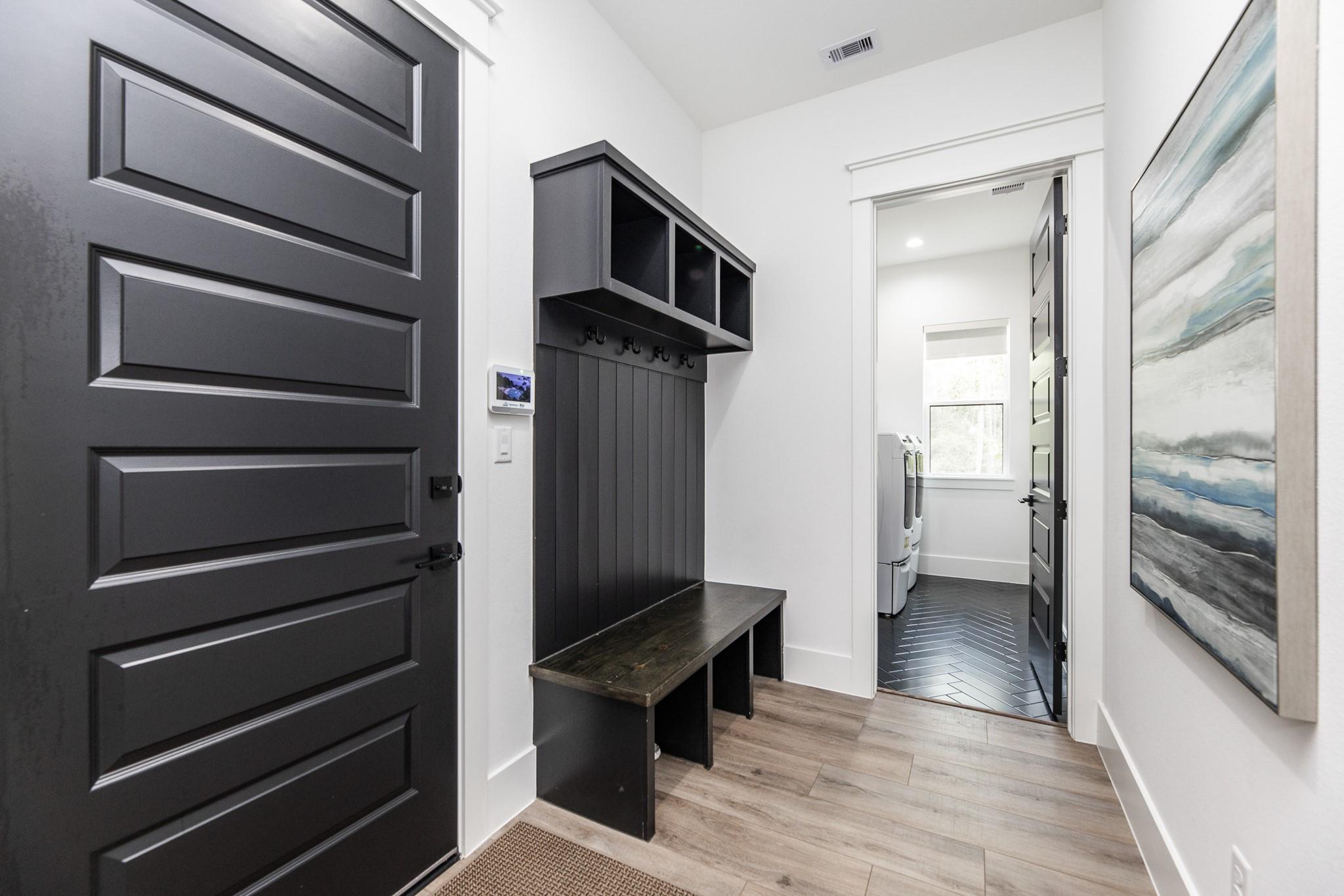 Entryway with a black built-in mudroom bench and hooks beside an open laundry room doorway.