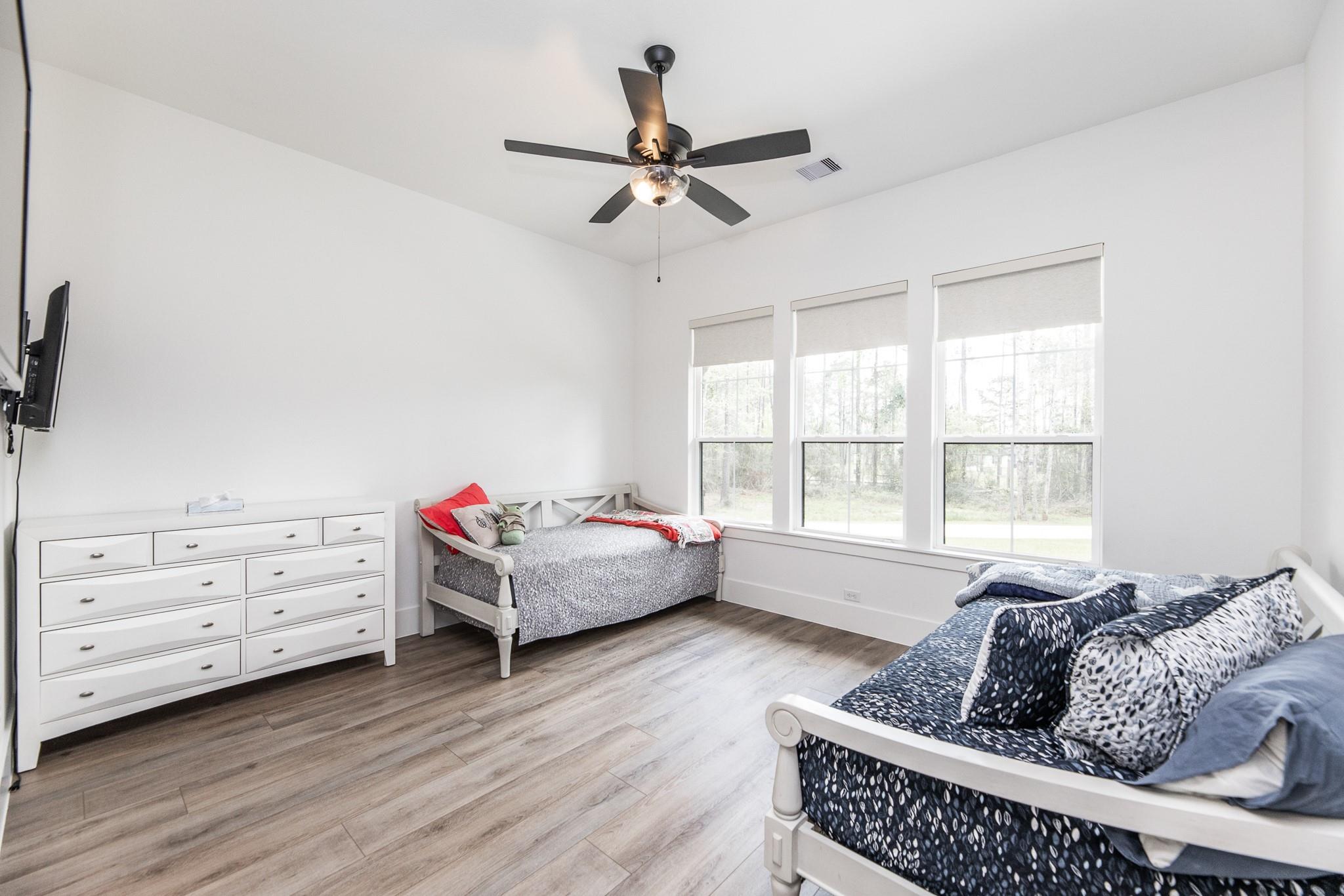 Bedroom with two white daybeds, a dresser, and three windows overlooking trees.