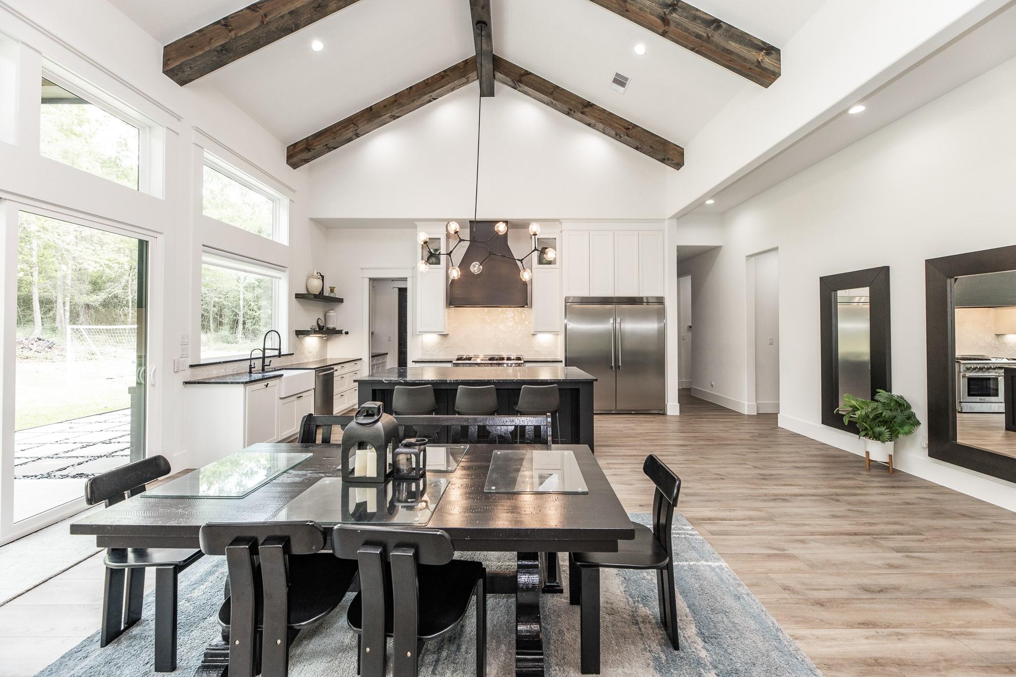 Open-plan kitchen and dining room with exposed wood beams, a dark island, and large windows.