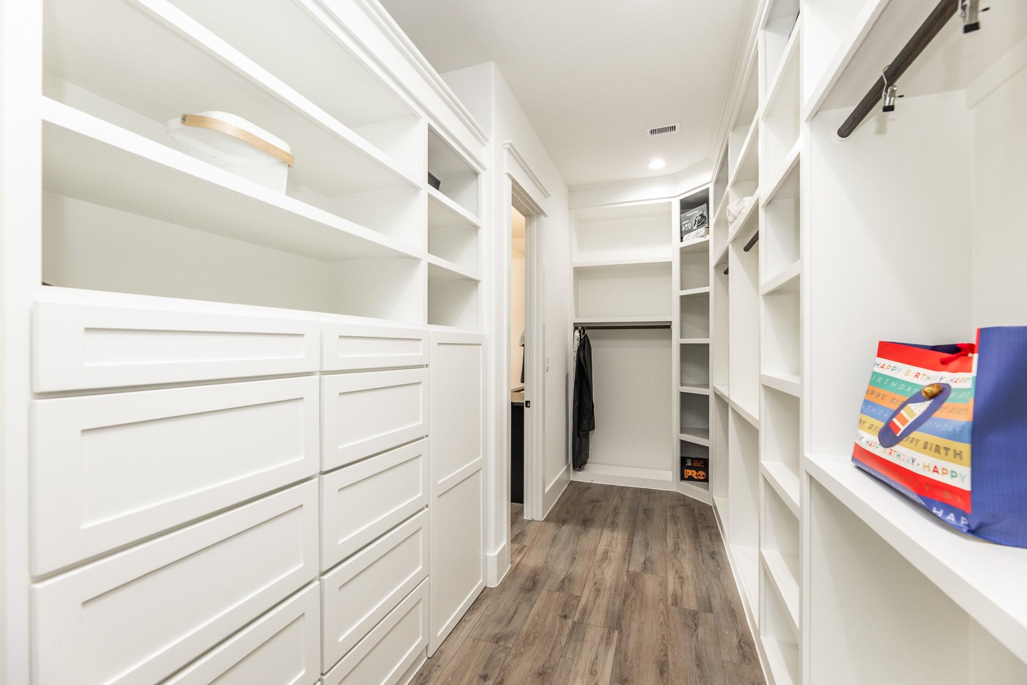 Walk-in closet with white built-in drawers, open shelving, hanging space, and wood-look flooring.