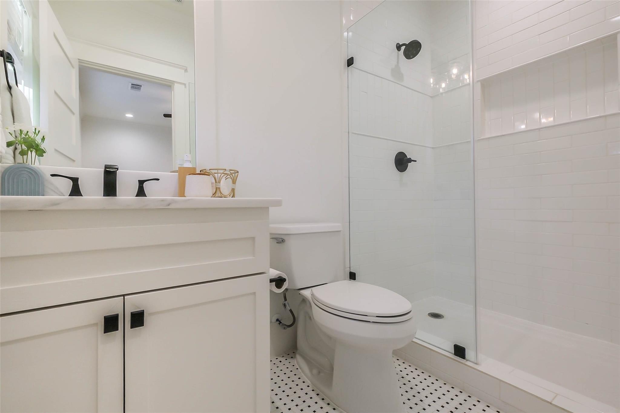 Bathroom with white vanity, black fixtures, glass shower, and black-and-white mosaic floor