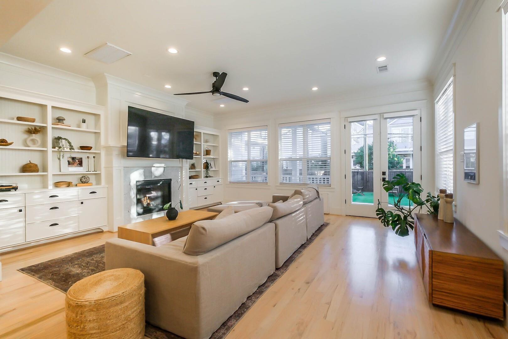 Bright living room with built-in shelving, a fireplace, beige sofas, and glass doors to a patio.