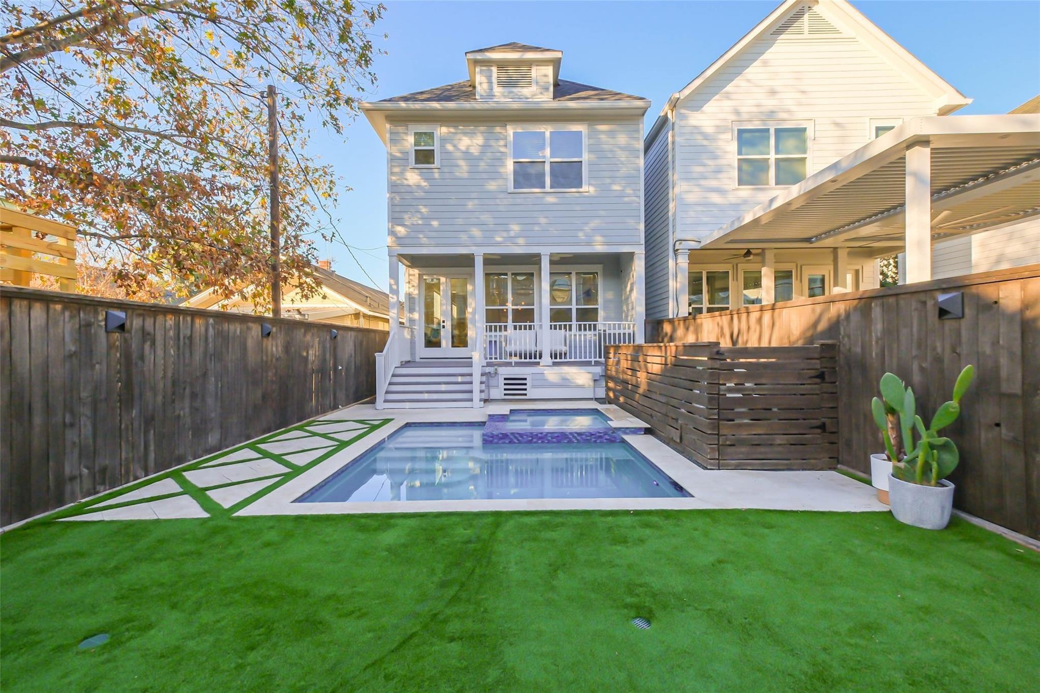 Backyard pool and covered patio behind a two-story house, surrounded by fencing and artificial turf.