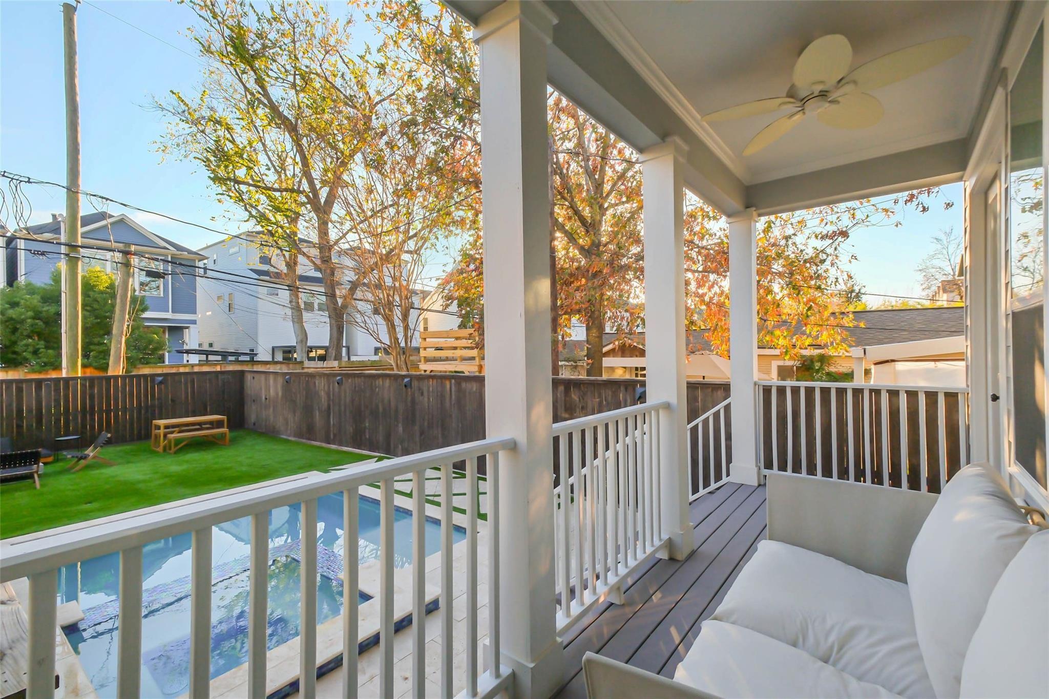 Covered porch with cushioned seating overlooks a swimming pool and fenced backyard.