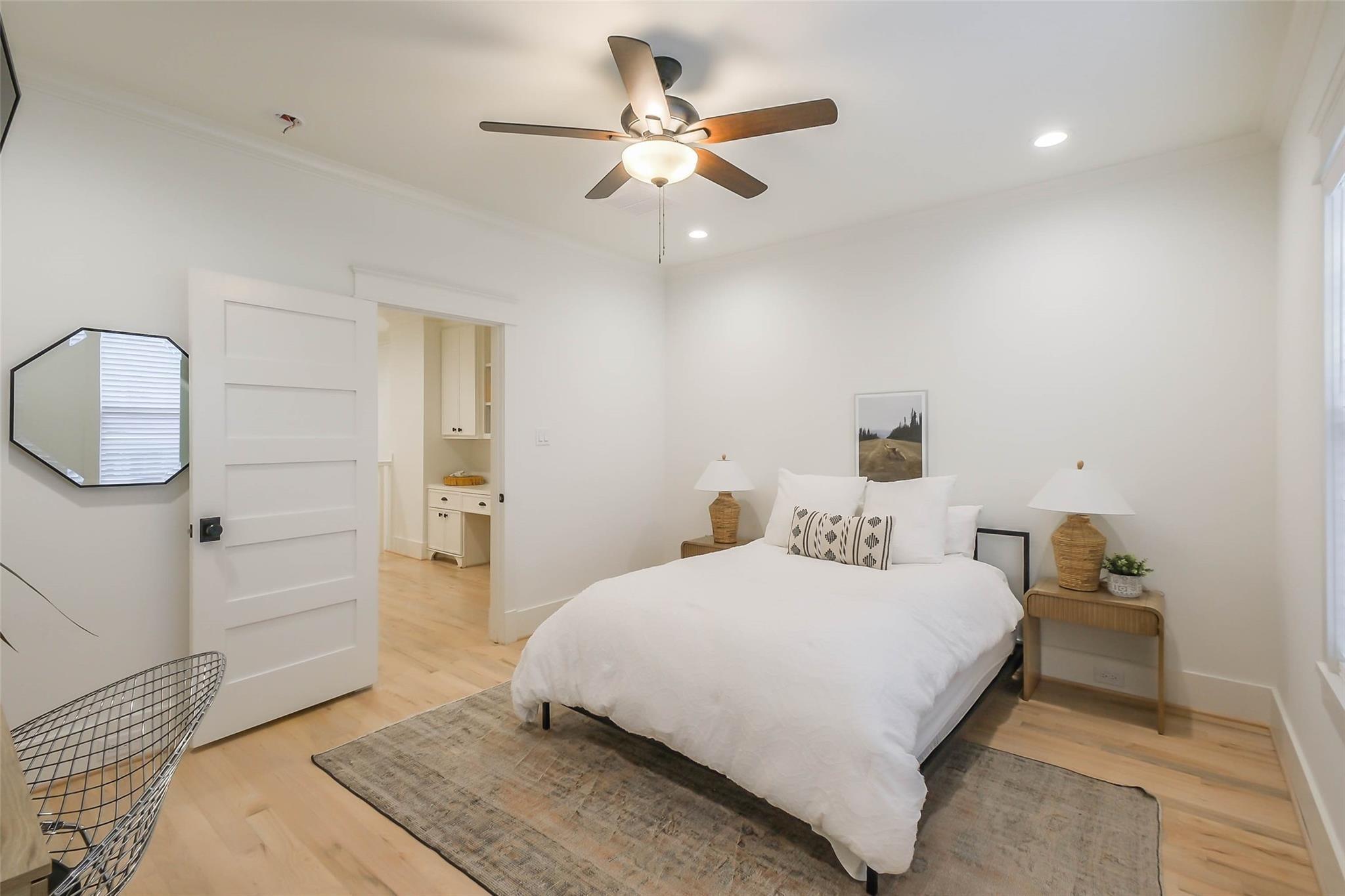 Bedroom with a white bed, ceiling fan, wood floors, and a sliding barn-style door.