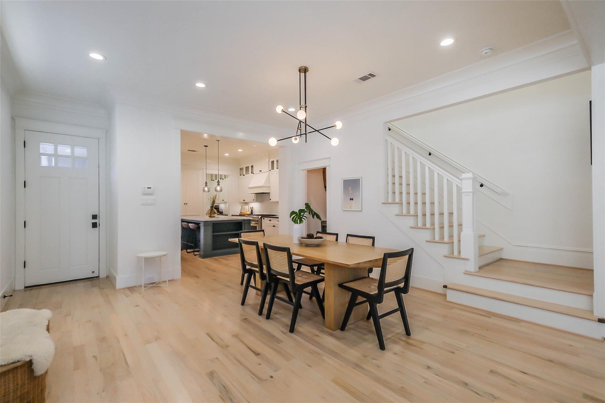 Dining room with a wood table, modern pendant, open kitchen, and white staircase.