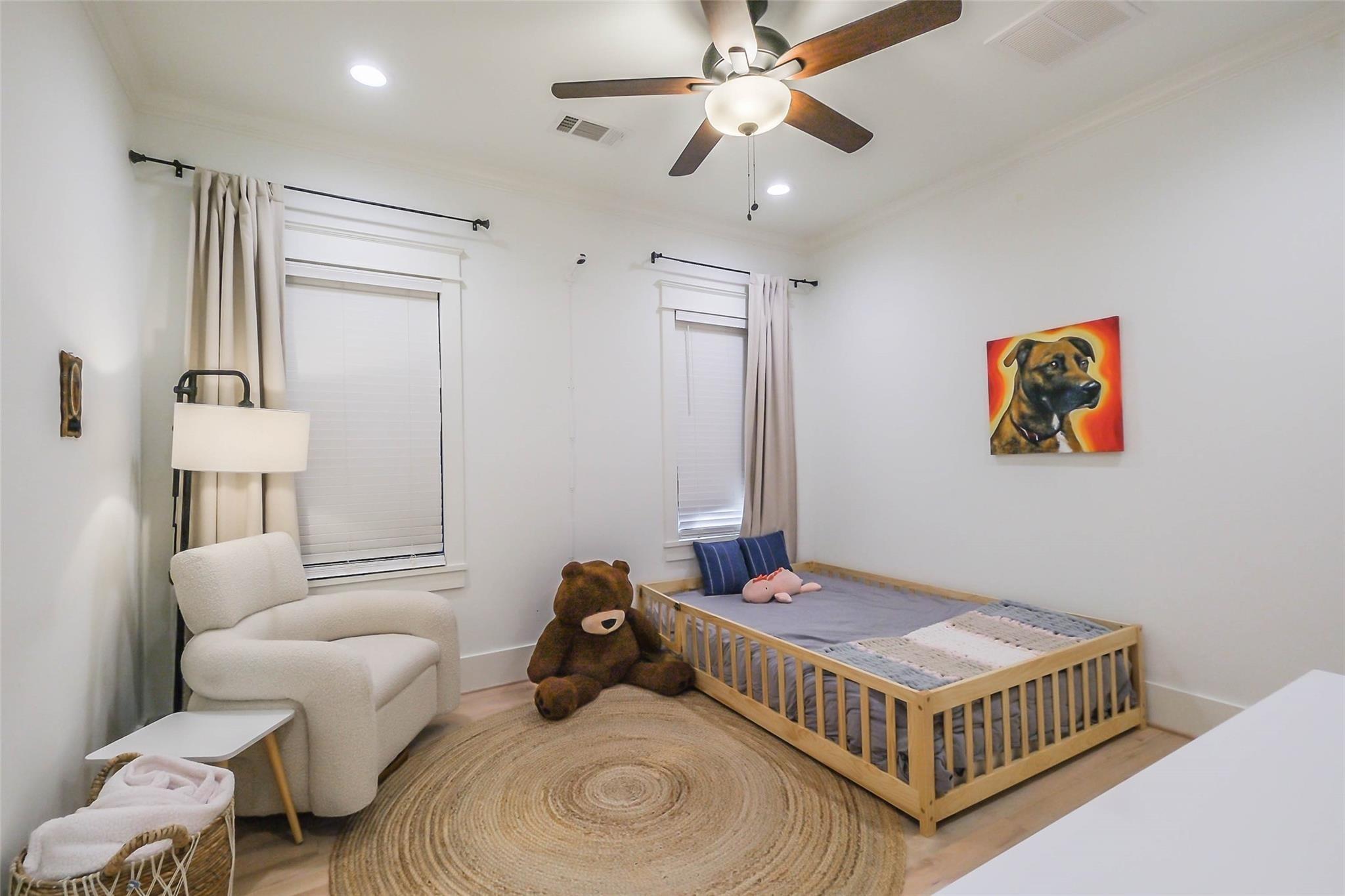 Nursery bedroom with a wooden toddler bed, oversized teddy bear, and white rocking chair.