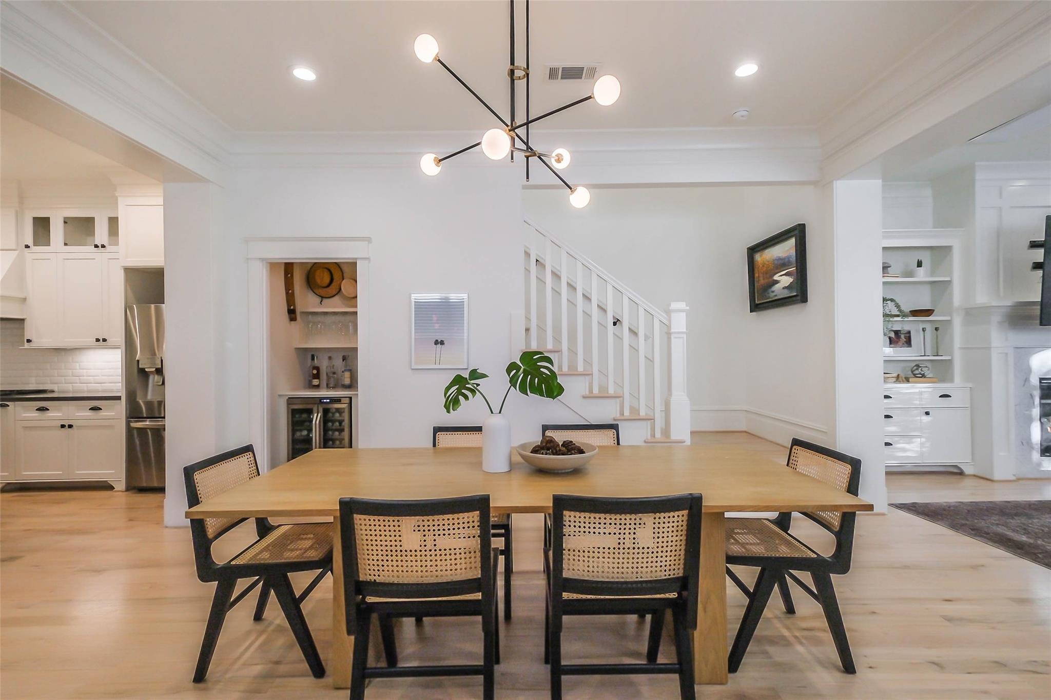 Dining room with a long wood table, cane-back chairs, globe chandelier, and staircase.