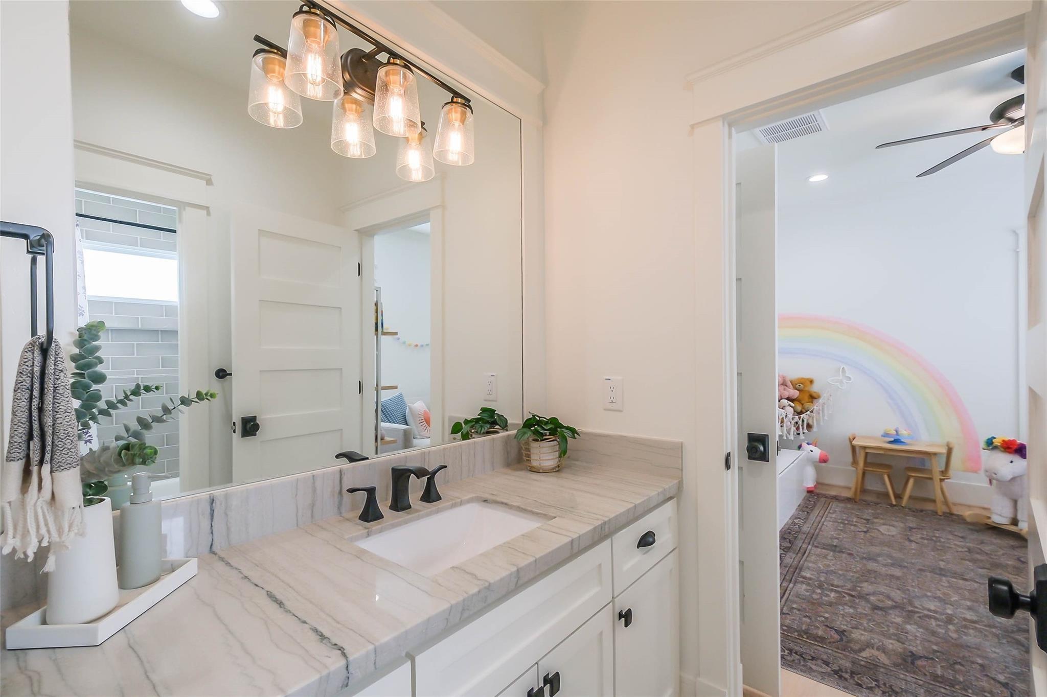 Bathroom vanity with a marble countertop and black fixtures, opening onto a child’s room with a rainbow mural.