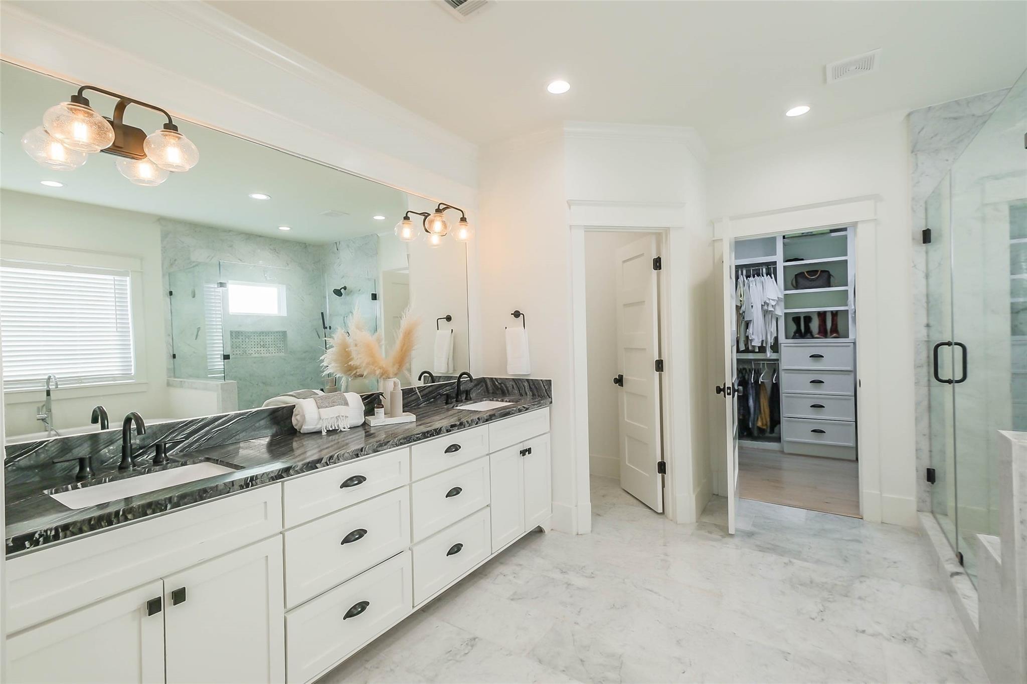 Primary bathroom with a double vanity, dark stone counters, marble shower, and open walk-in closet.