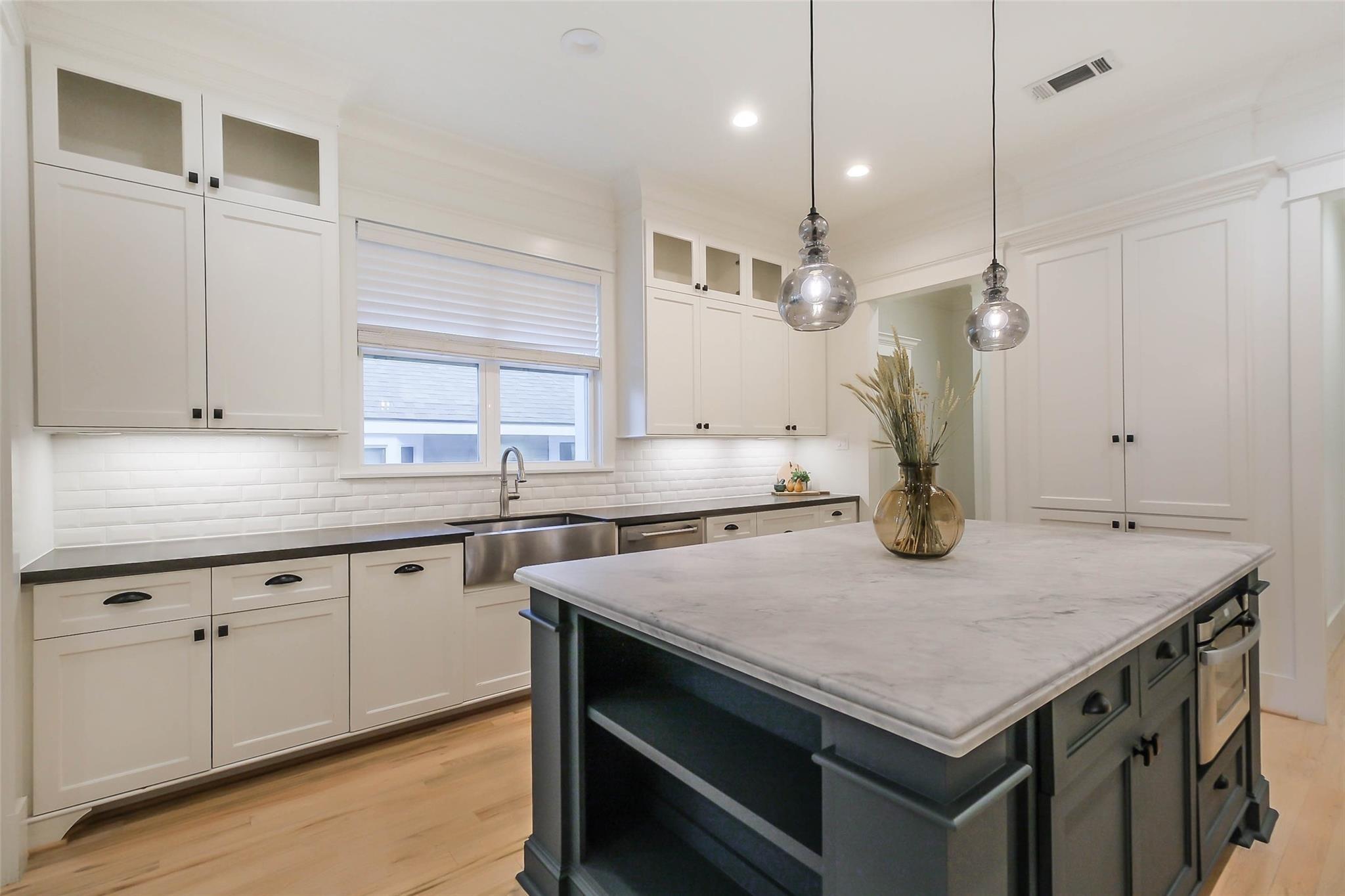 Kitchen with white cabinets, subway tile backsplash, and a large dark island with a pale stone countertop.
