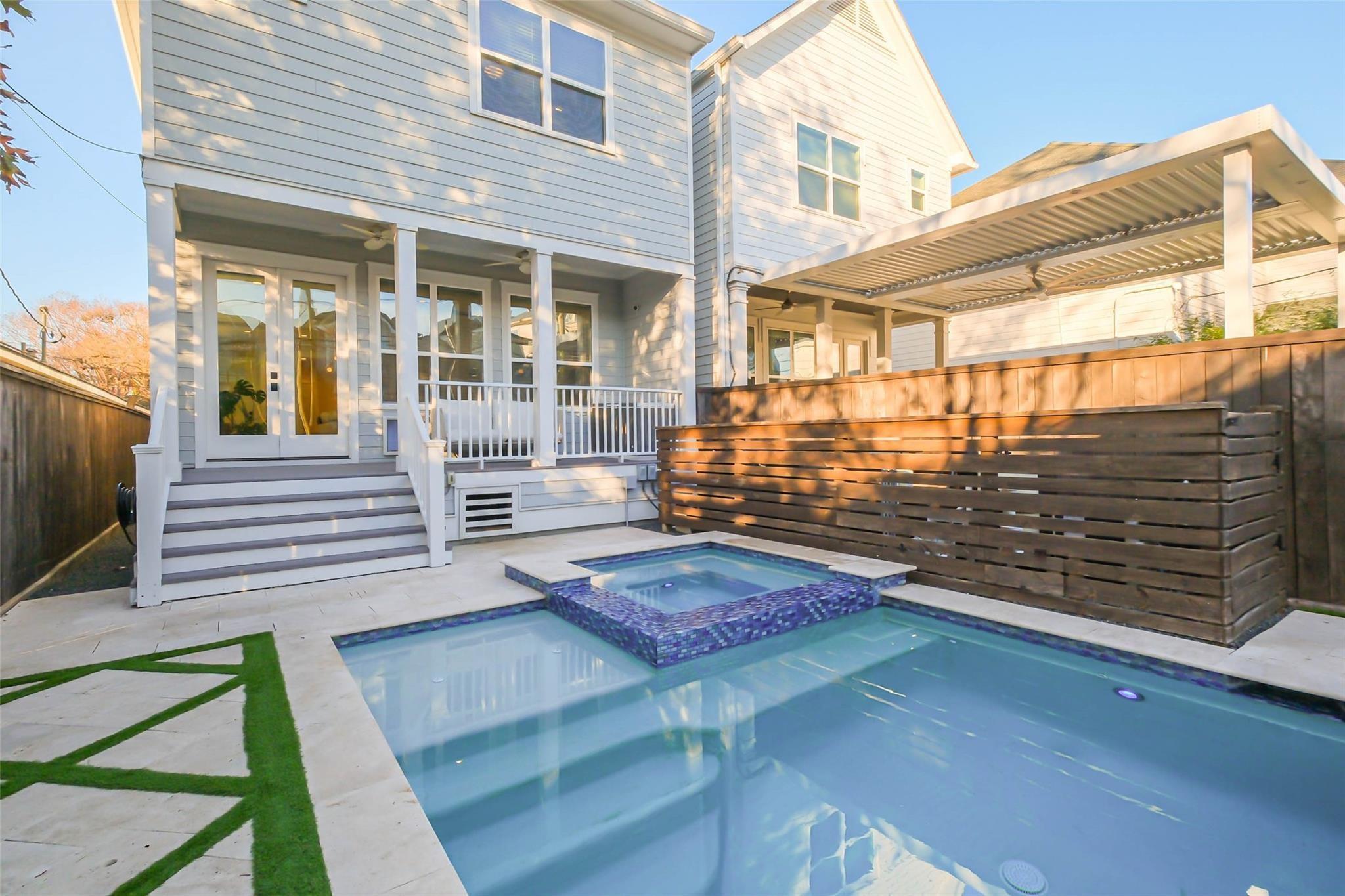 Backyard pool and raised tiled spa beside a white two-story house and covered porch.