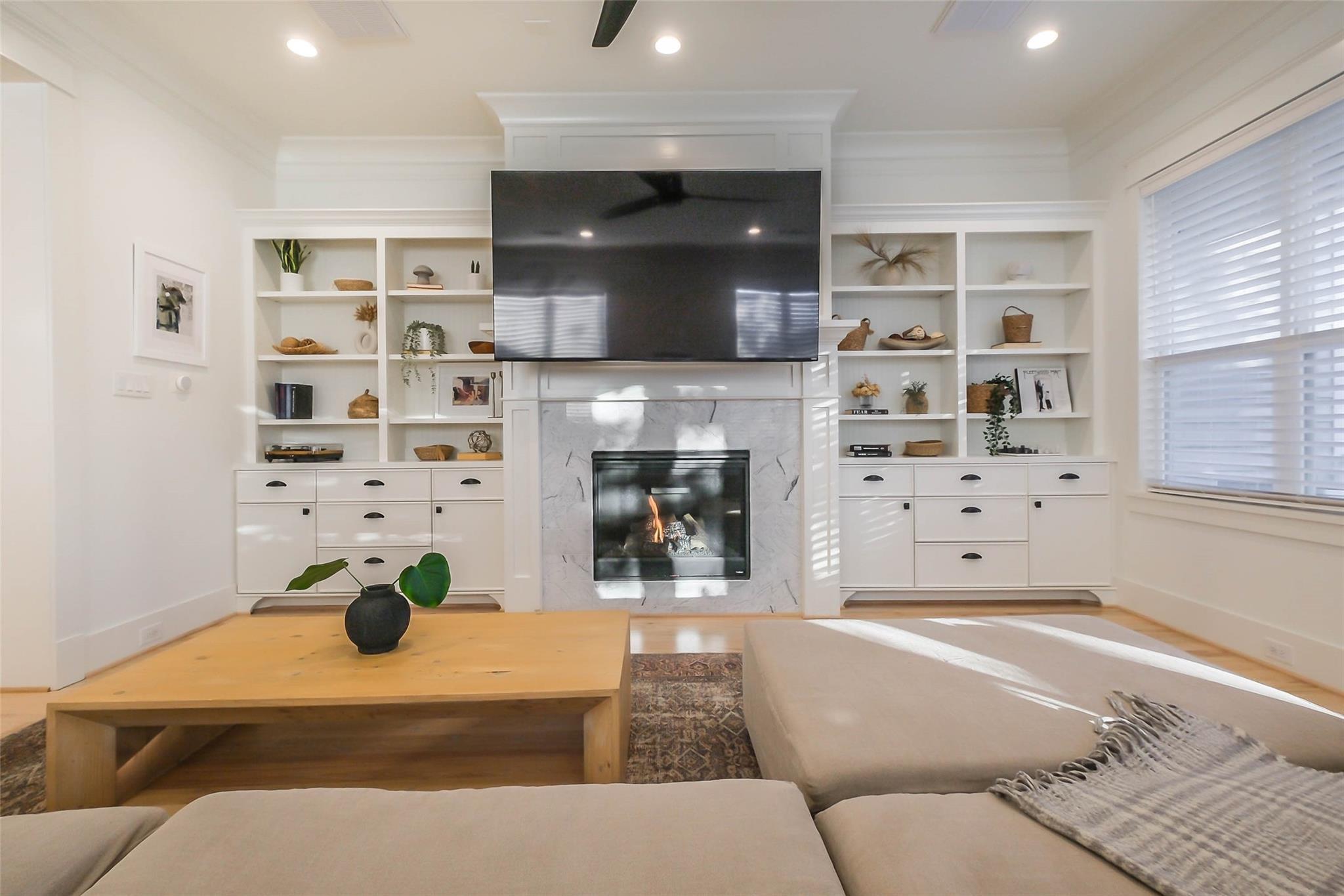 Living room with a marble fireplace, built-in shelving, wall-mounted TV, and sectional sofa.