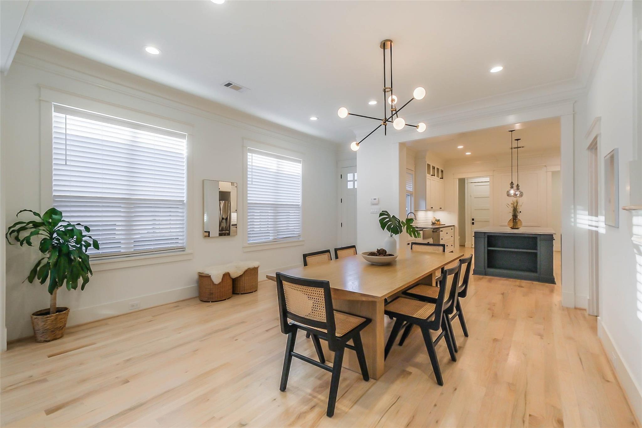 Dining room with a long wood table, cane-back chairs, pale floors, and kitchen beyond.