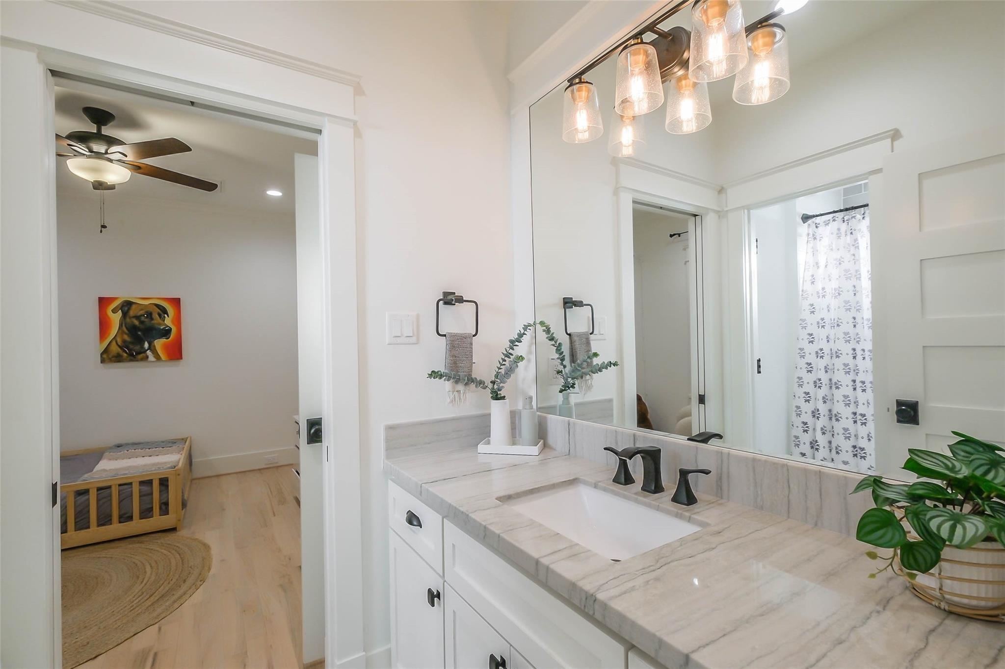 Bathroom vanity with a veined stone counter and glass pendant lights, opening onto a bedroom with a wooden bed.