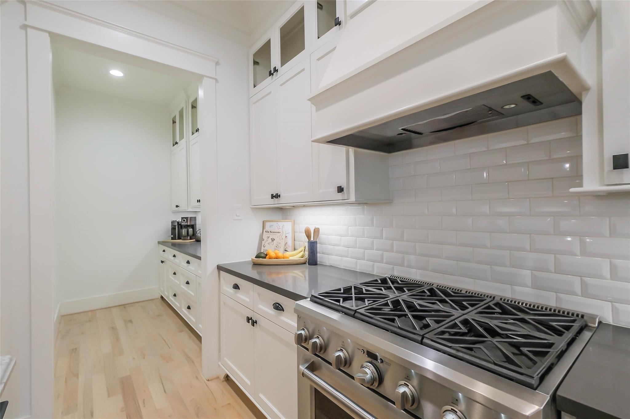White kitchen with a stainless-steel gas range, subway-tile backsplash, and light wood floors.