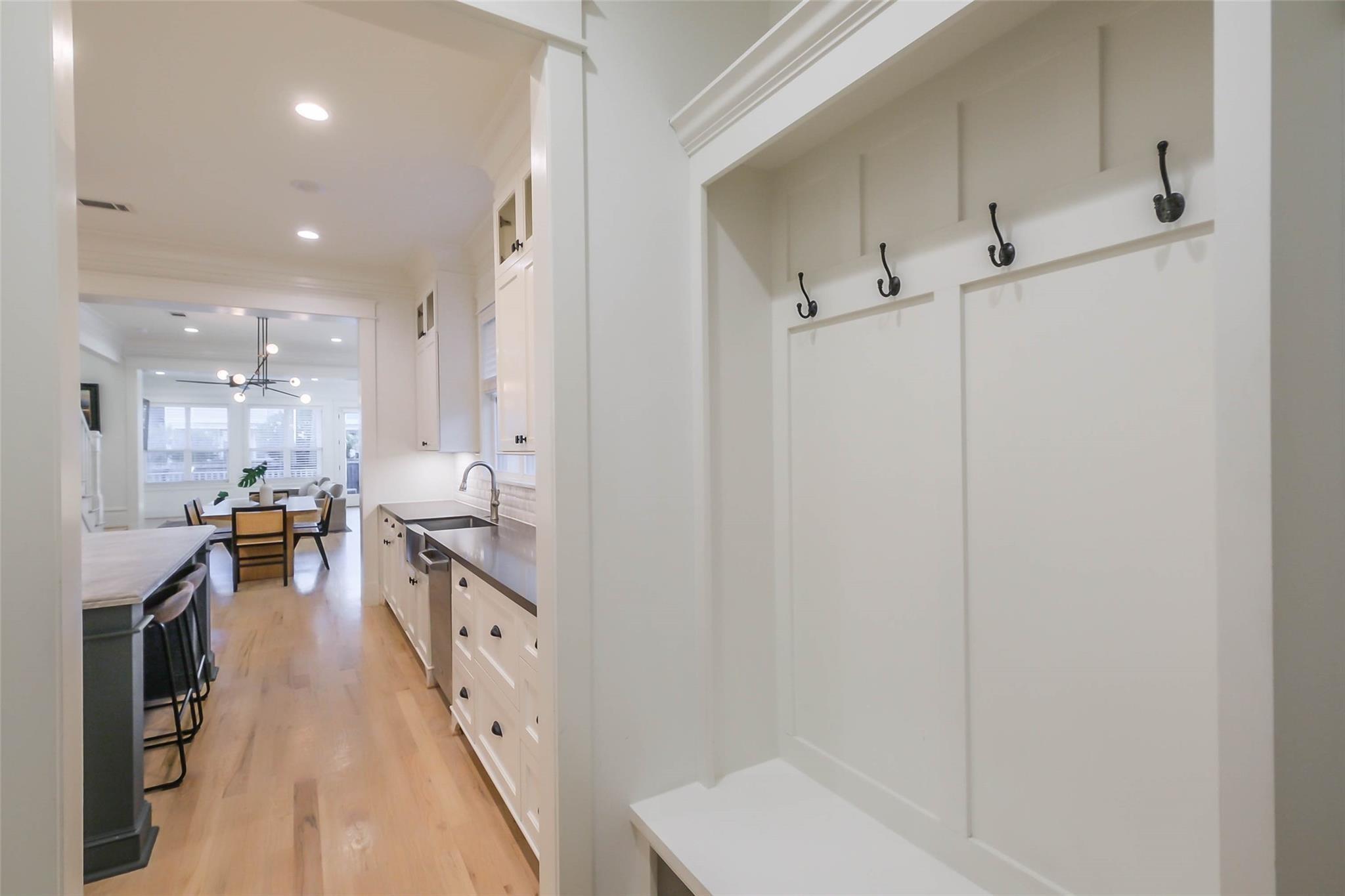 Mudroom bench with black hooks overlooking a bright kitchen and dining area.