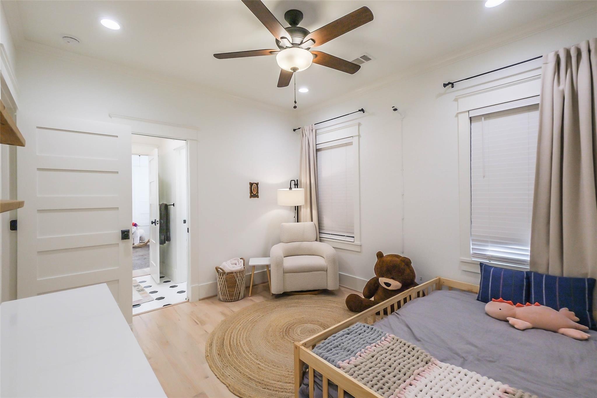 Bedroom with a wooden toddler bed, plush toys, woven rug, and cream armchair.
