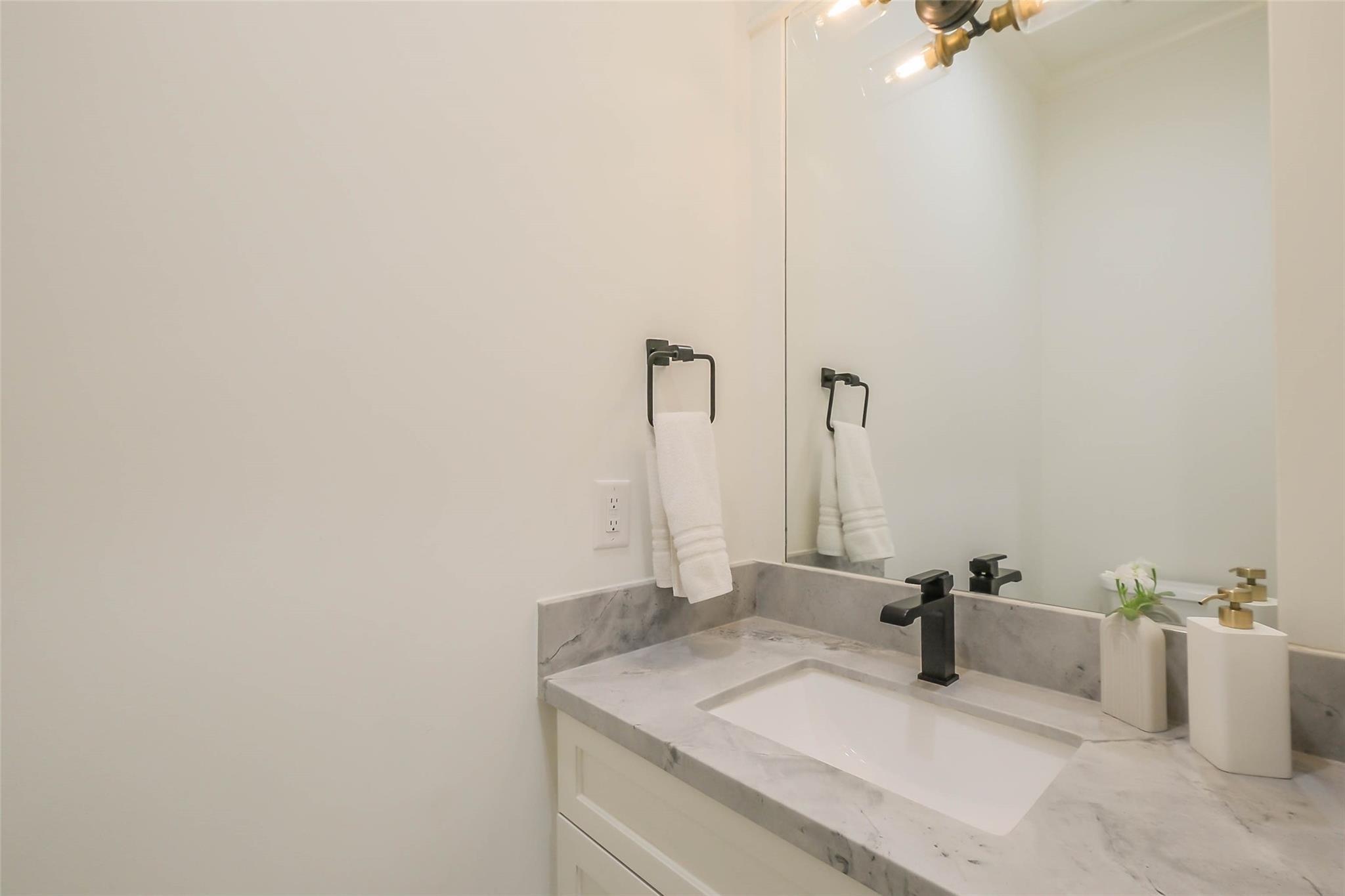 Bathroom vanity with a gray-veined marble counter, white sink, black faucet, and large mirror.