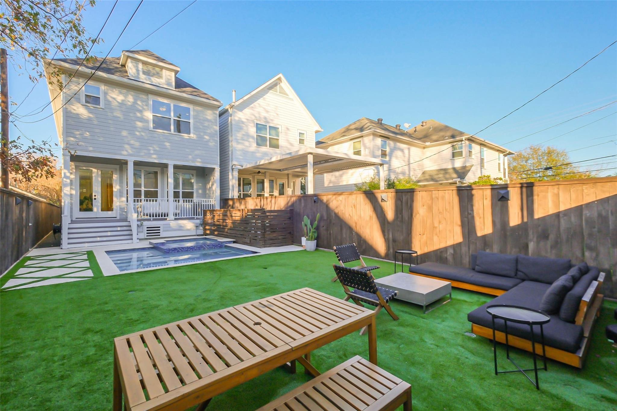 Backyard with a small pool, artificial turf, and outdoor lounge seating beside a white house.