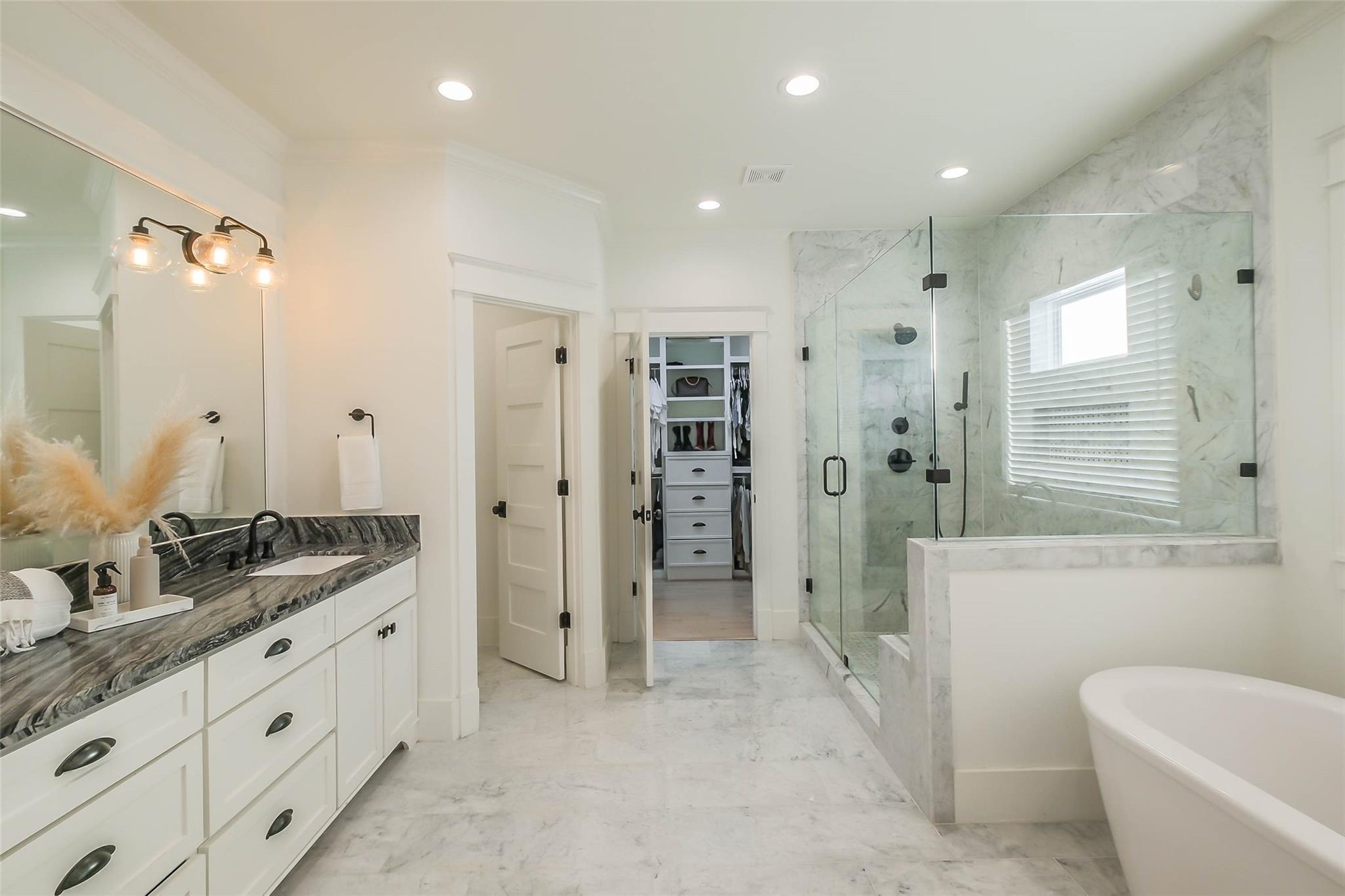 Bathroom with marble walk-in shower, freestanding tub, and white vanity with dark stone countertop.