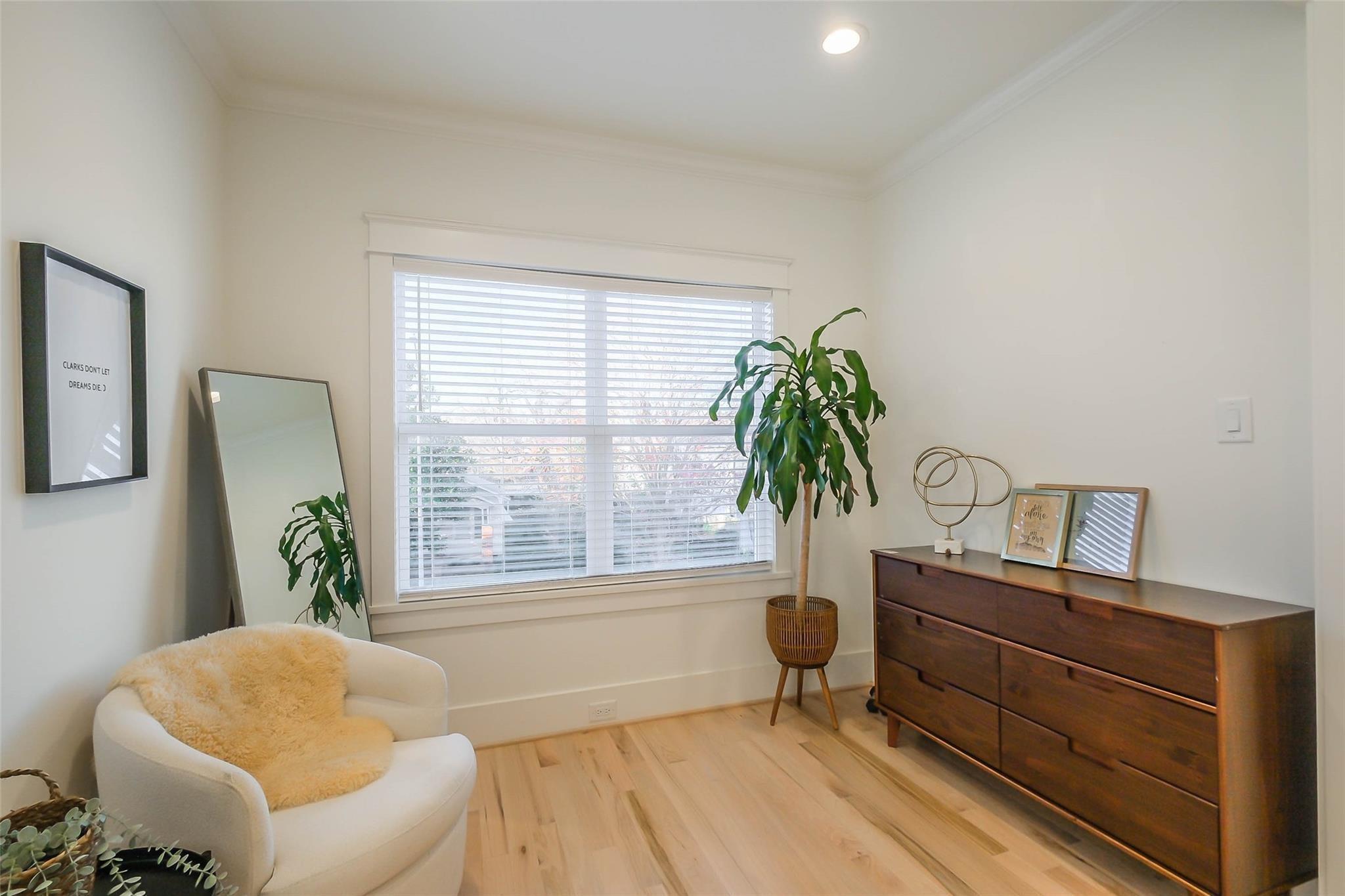 Living room corner with a white armchair, large window, potted plant, and dark wood dresser.