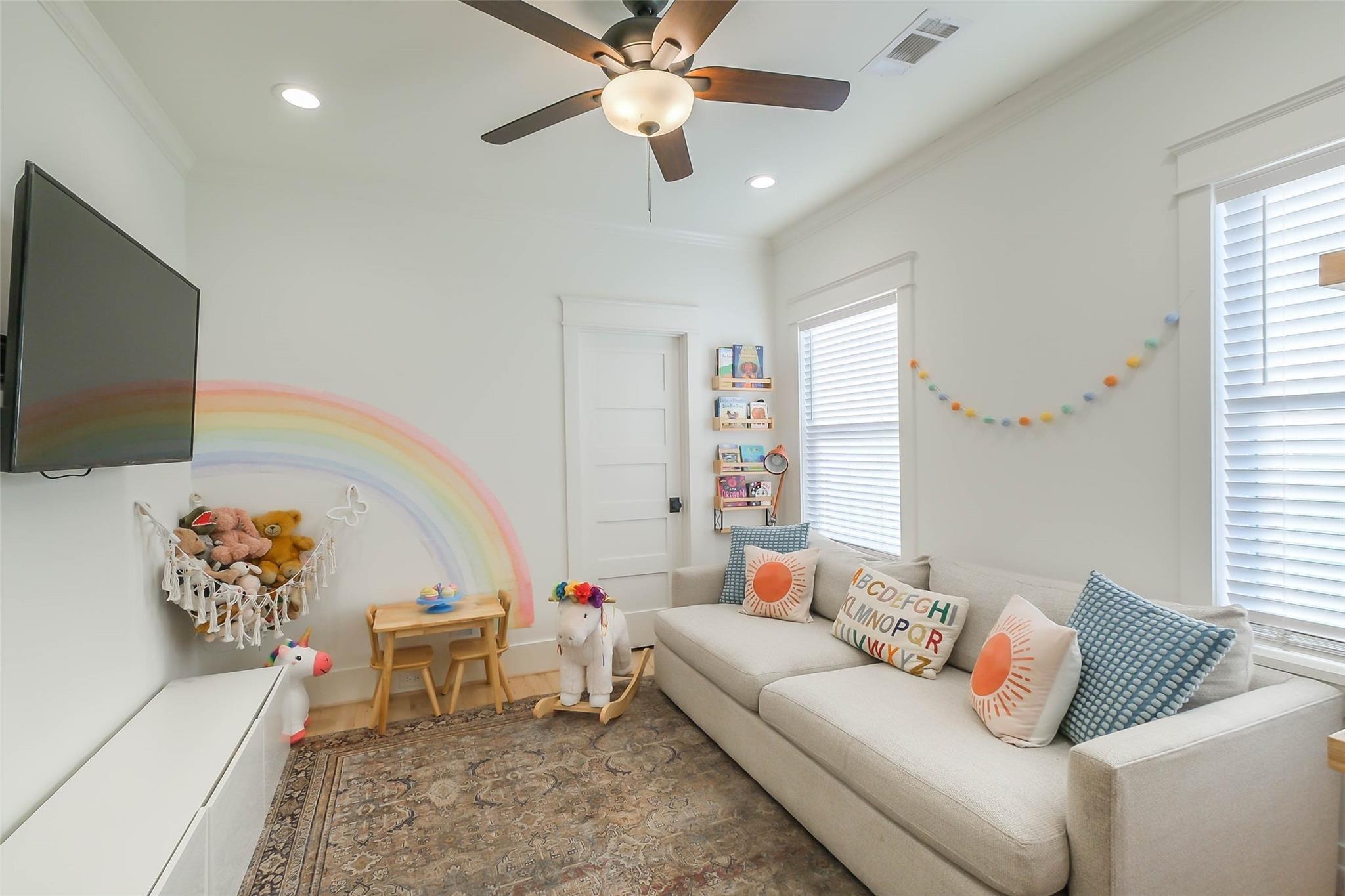 Bright playroom with a sectional sofa, pastel rainbow mural, toy hammock, and small wooden table.