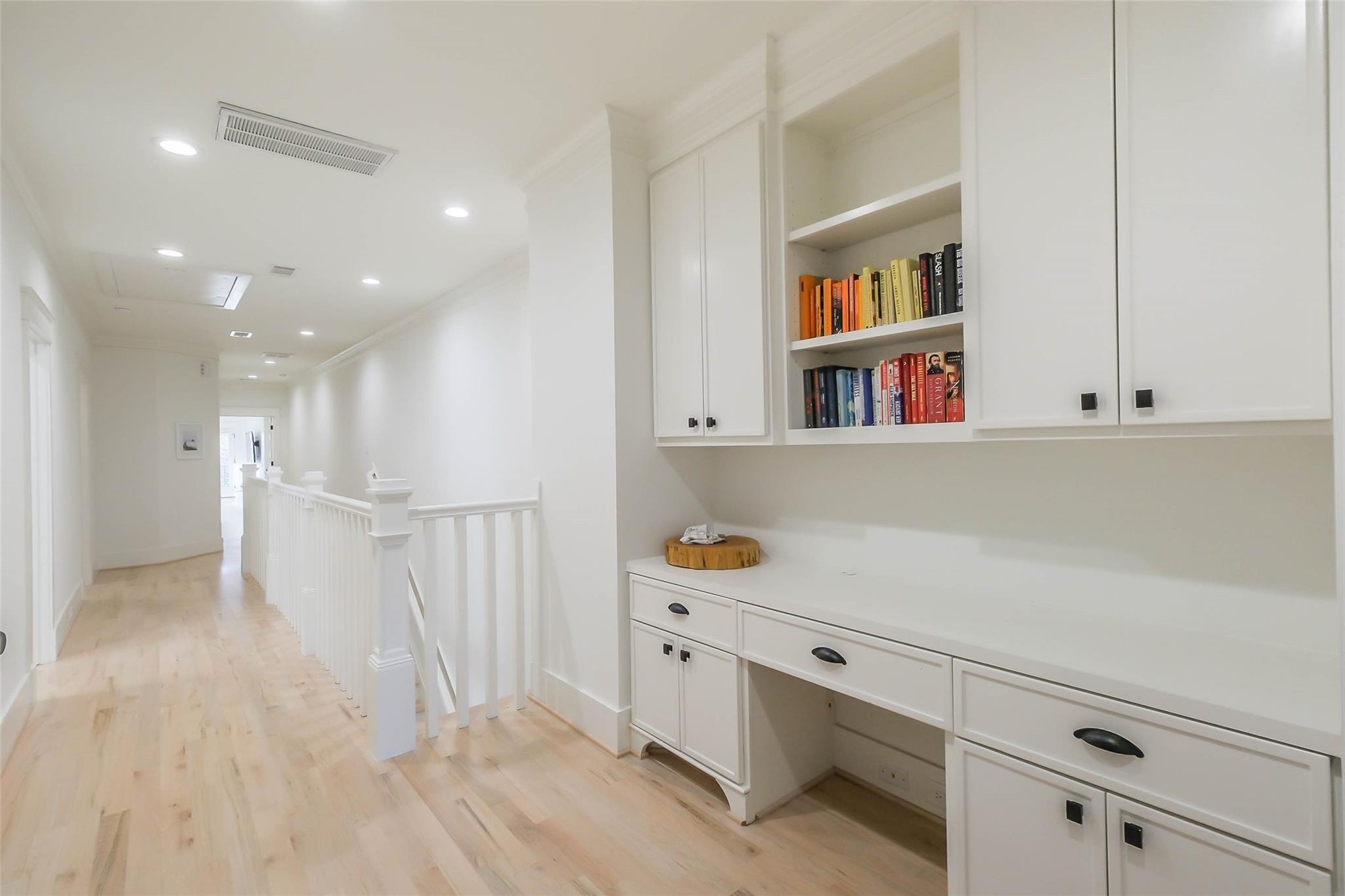 Upstairs hallway with a built-in white desk, book shelves, and stair railing.