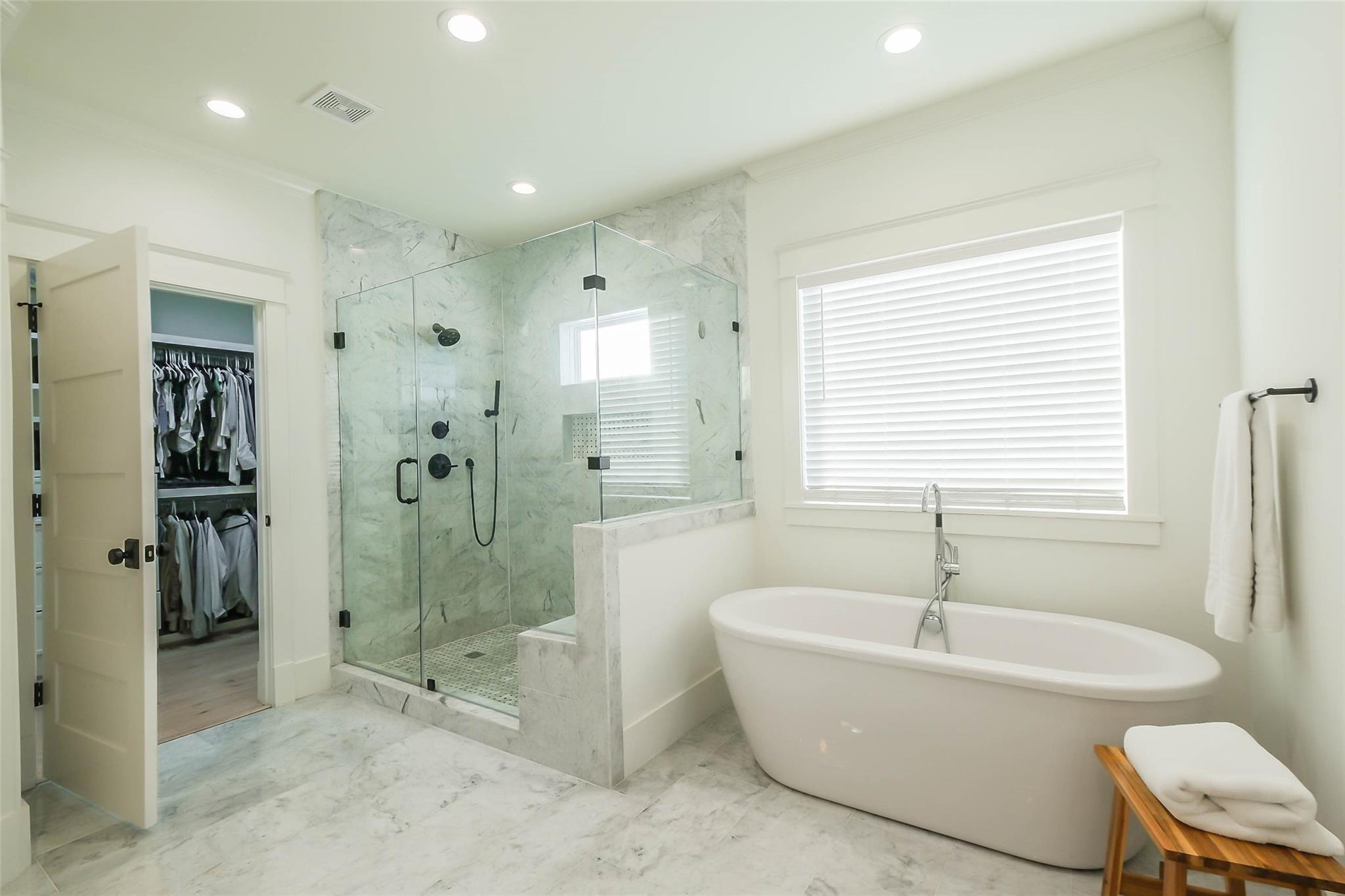 Primary bathroom with a freestanding soaking tub, glass-enclosed marble shower, and open walk-in closet.
